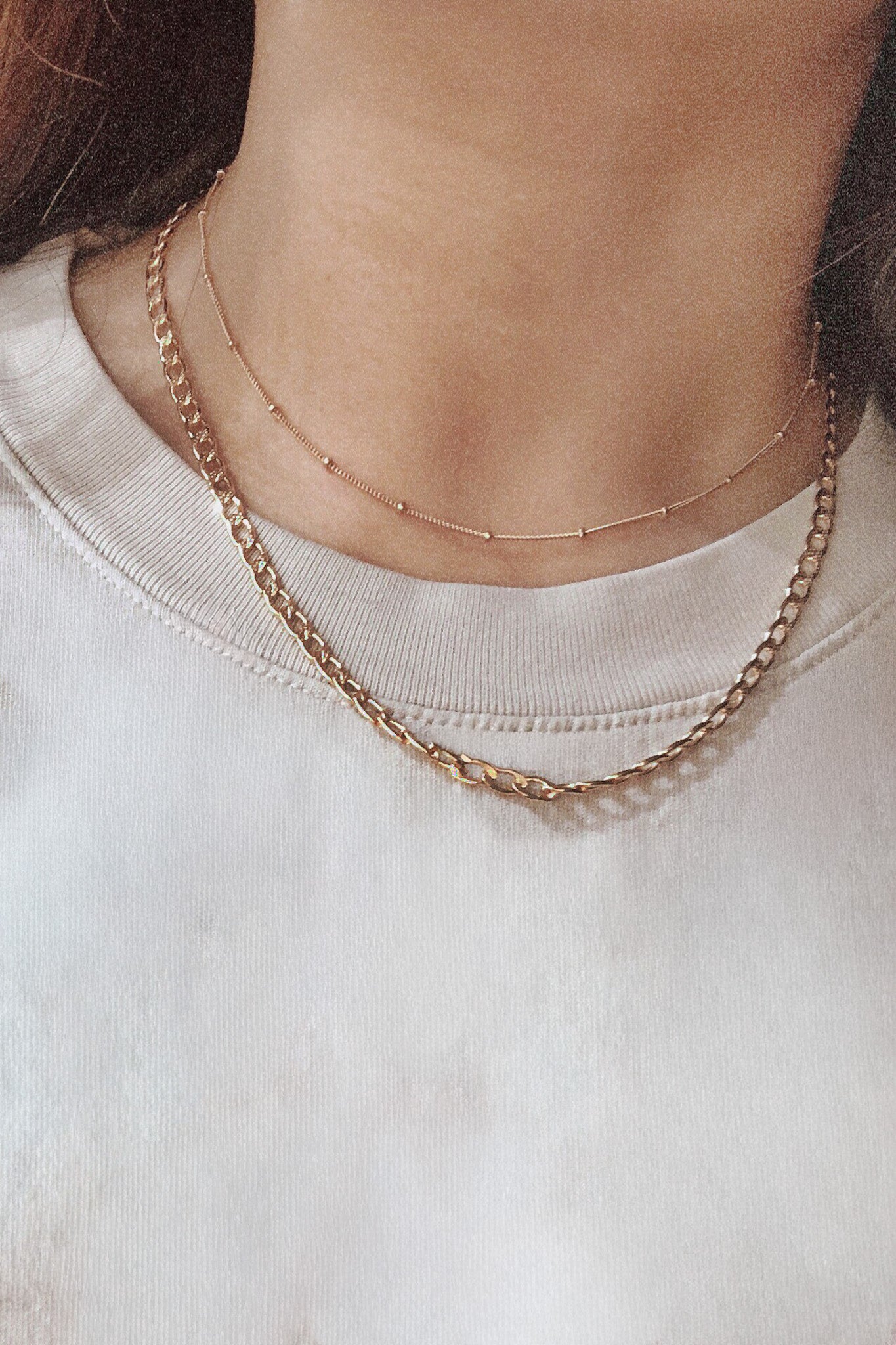 Gold chain necklace worn by a person on a white background