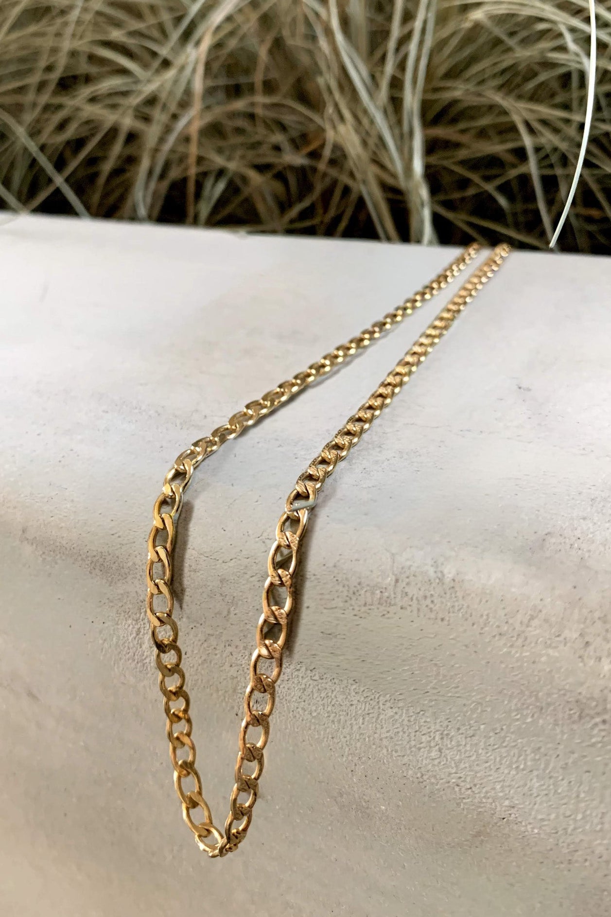 Gold chain necklace on a person's wrist with a natural background