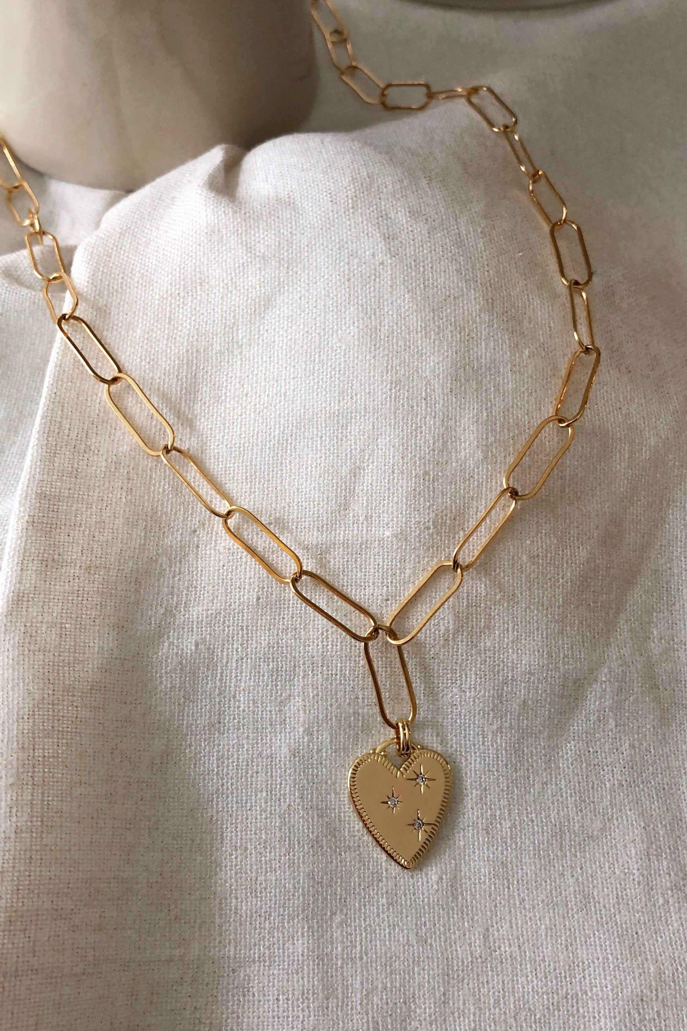 Gold chain necklace with a heart pendant on a light fabric background