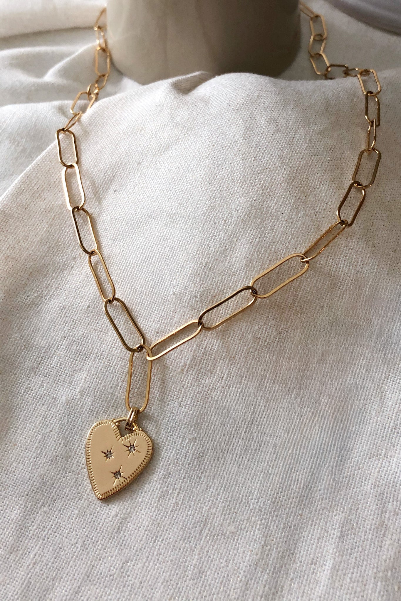 Gold chain necklace with a heart-shaped pendant on a light fabric background
