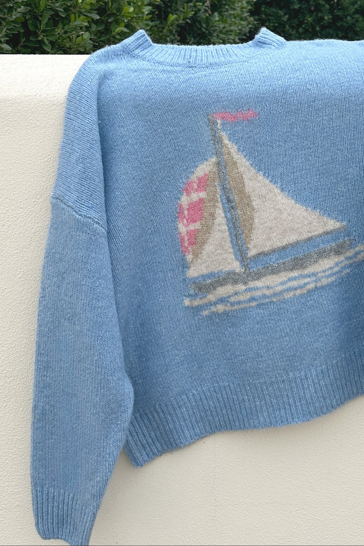Blue sweater with a sailboat design on a white surface