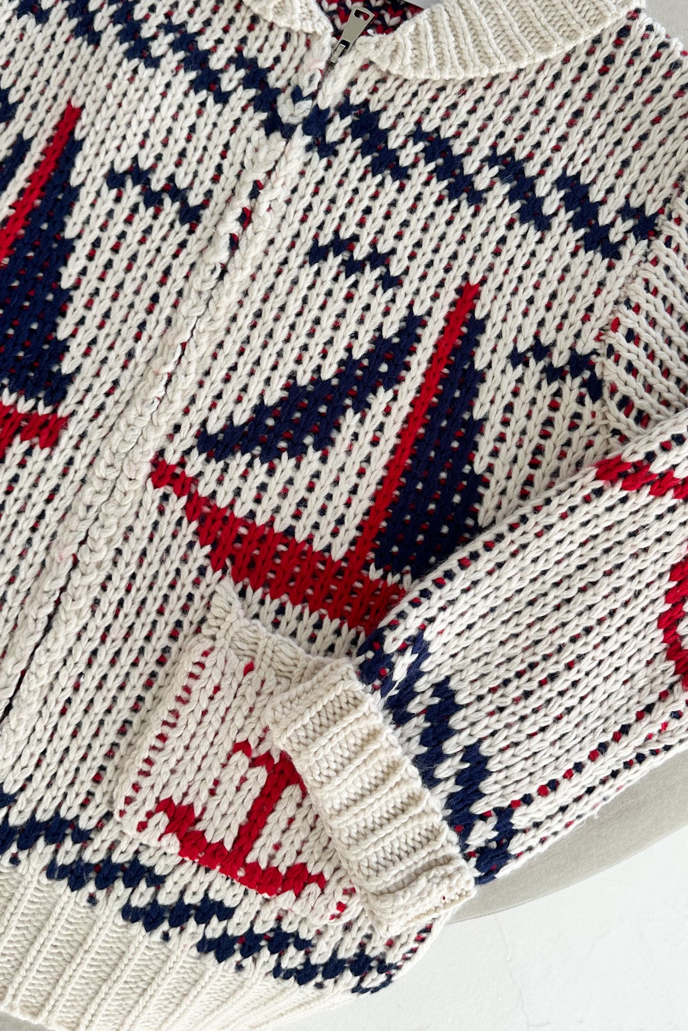 Close-up of a knitted sweater with red, blue, and white pattern on a white background