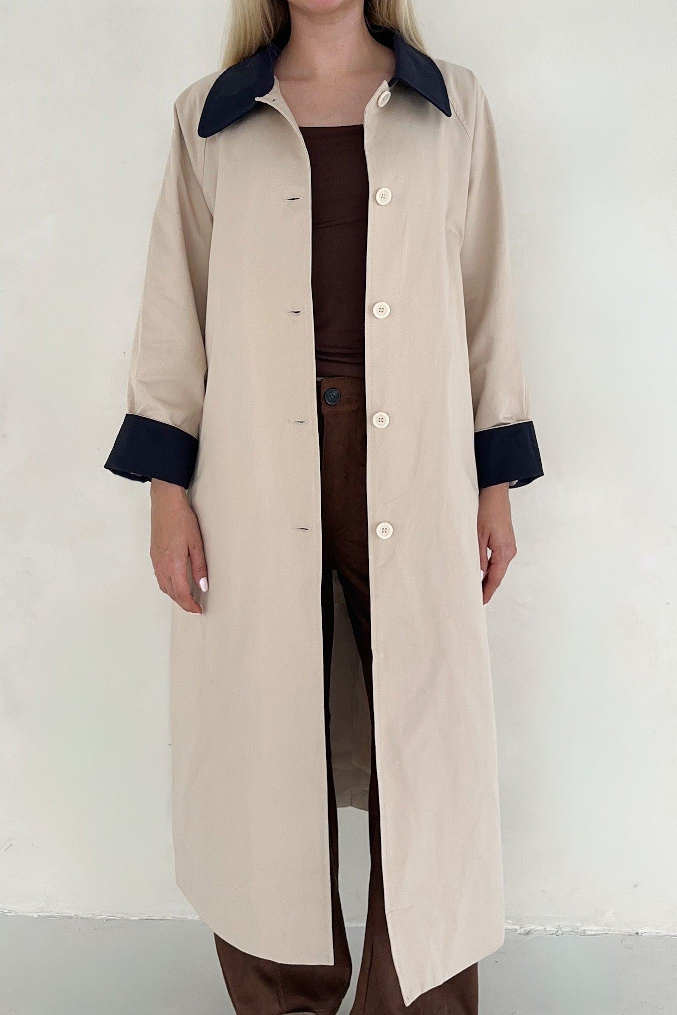 Person wearing a beige trench coat with navy trim on a white background