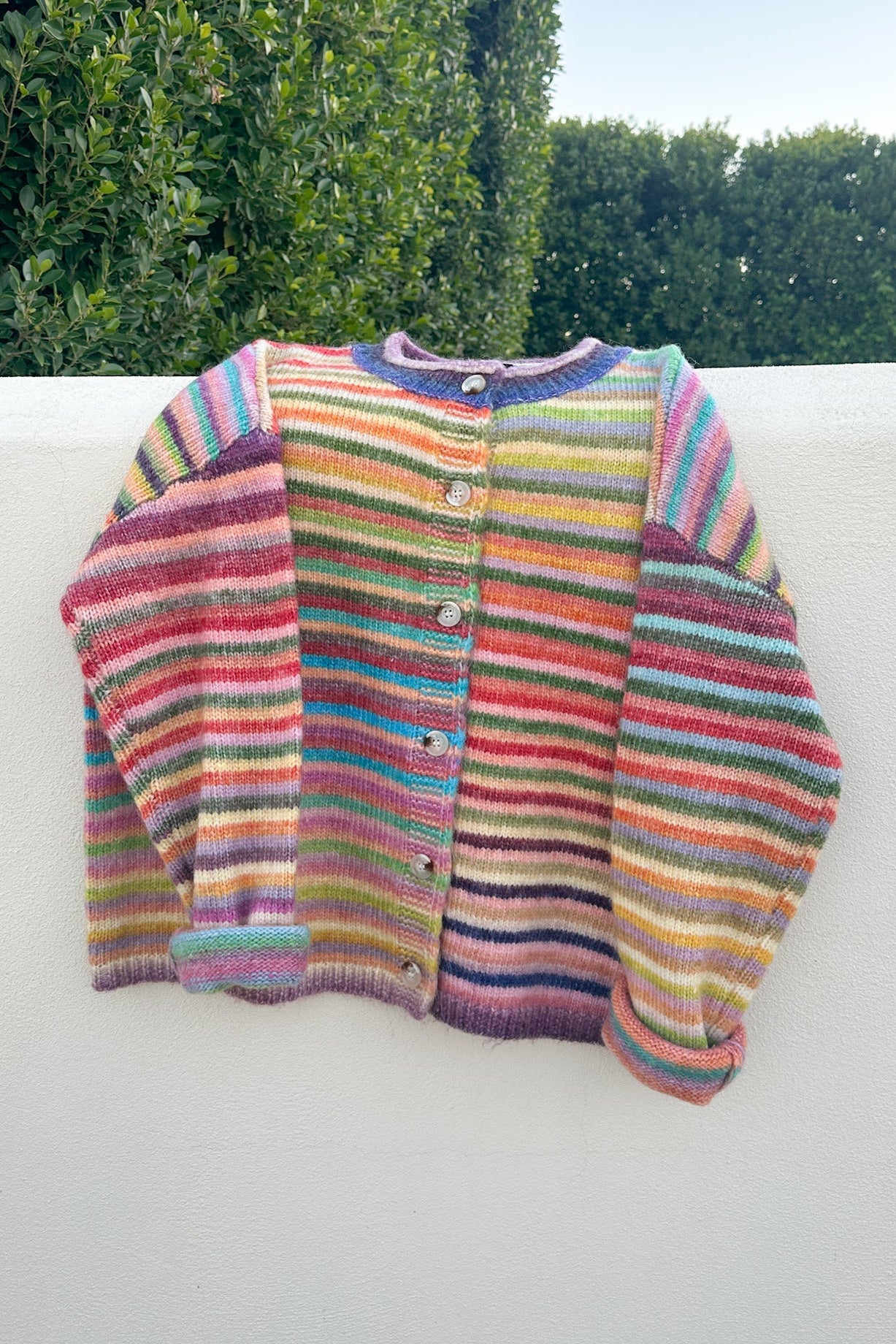 Multicolored striped sweater on a white surface with greenery in the background