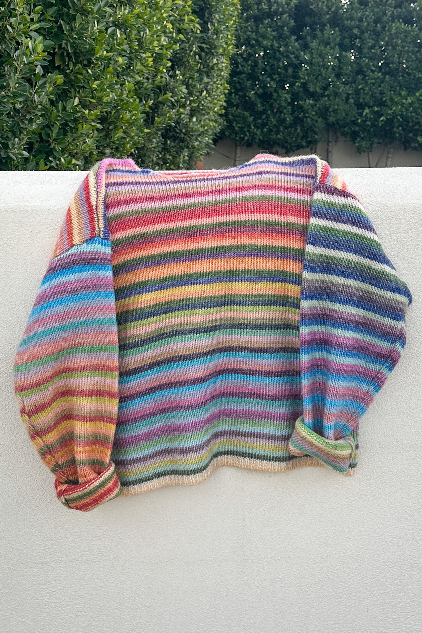 Multicolored striped sweater on a white surface with greenery in the background