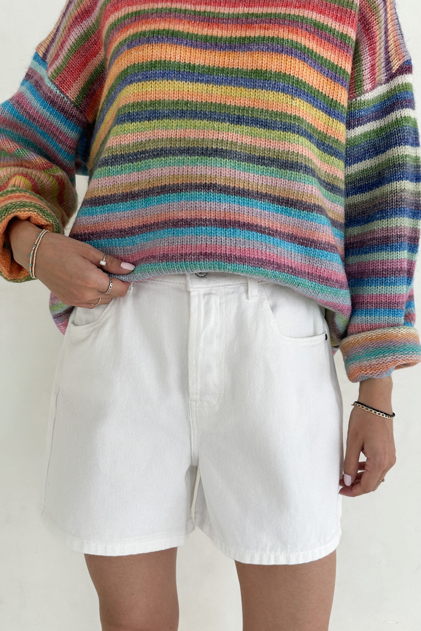 Person wearing a colorful striped sweater and white shorts on a plain background