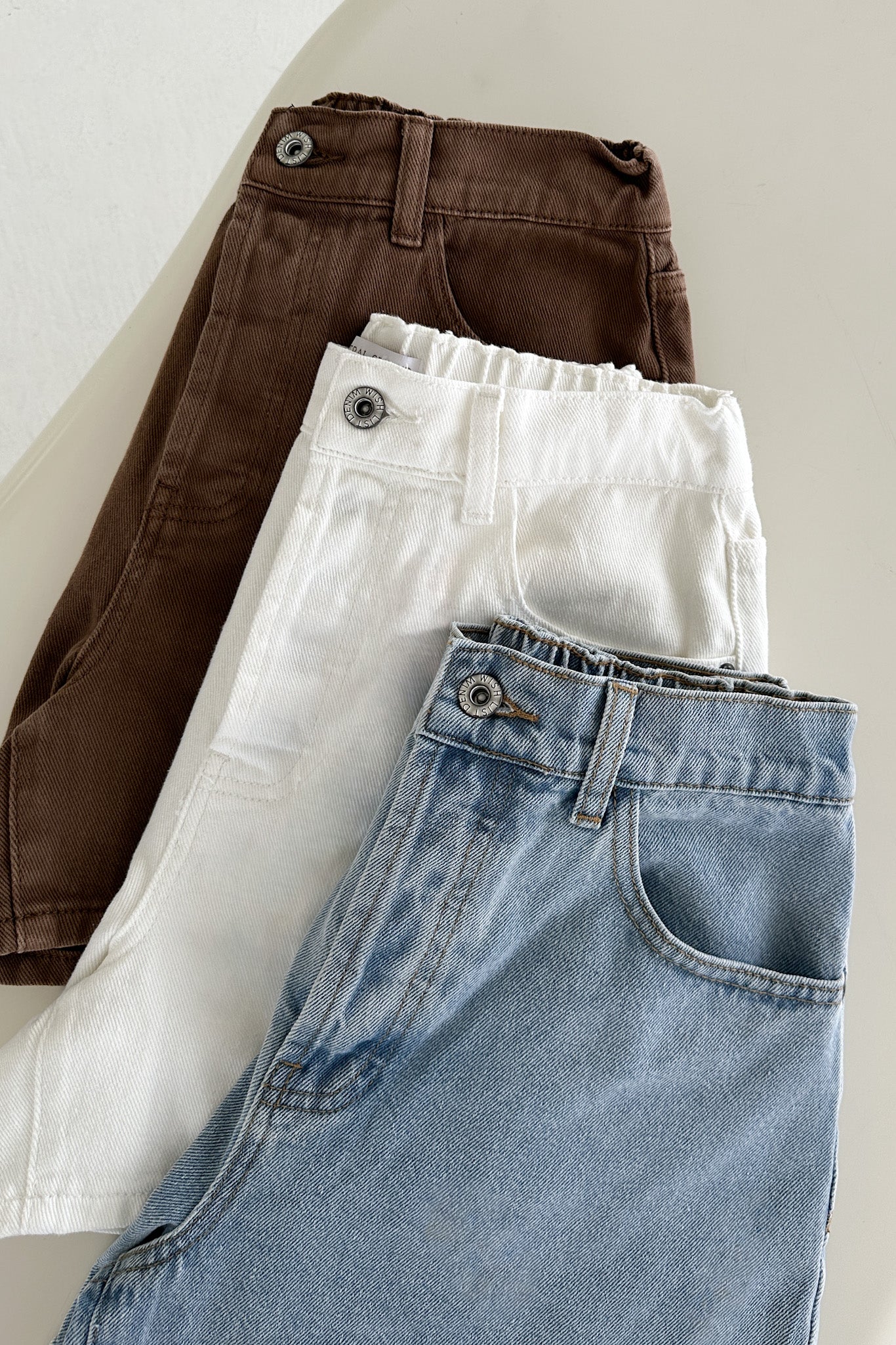 Three pairs of jeans in brown, white, and blue on a light background