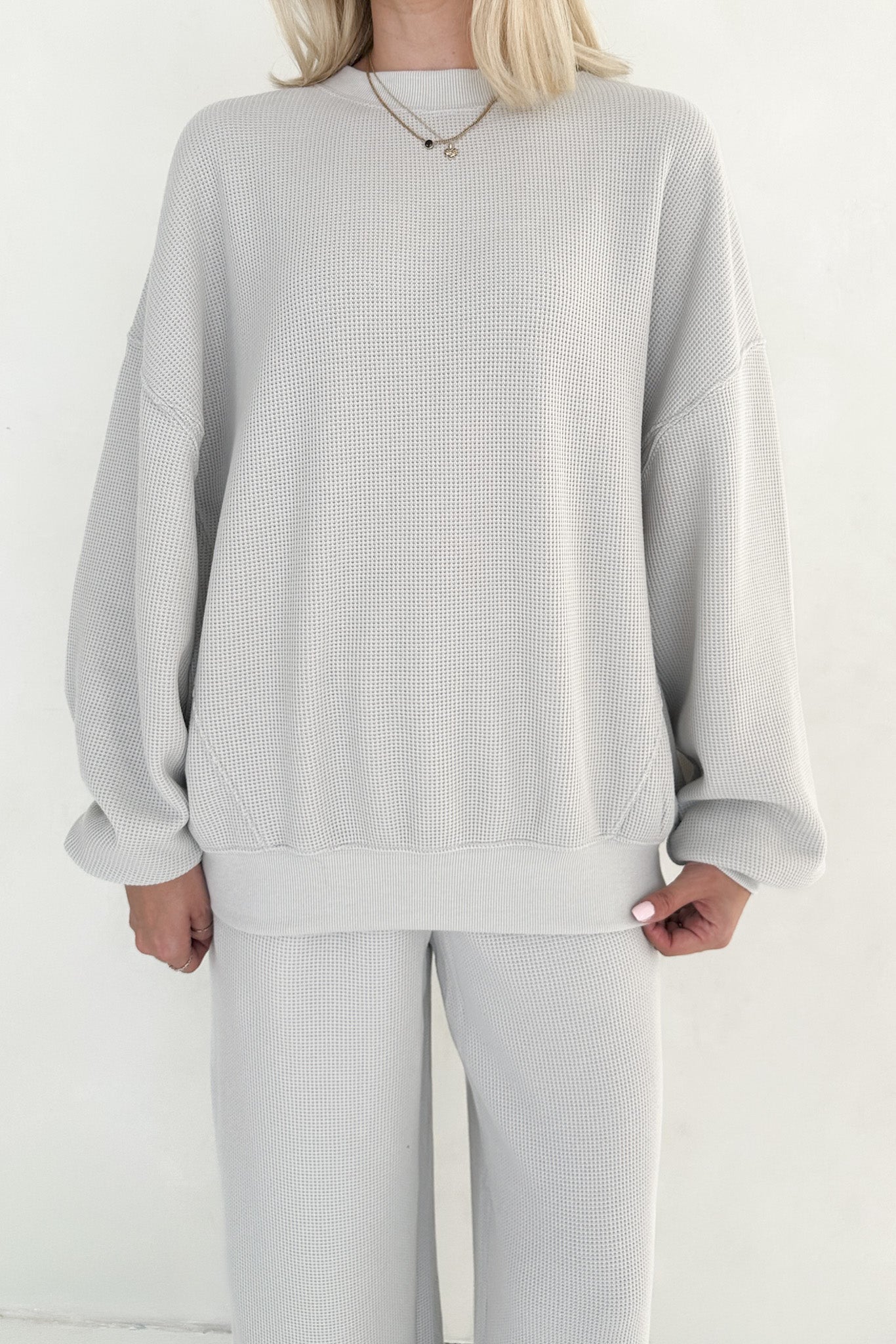 Person wearing a light gray ribbed sweater and pants on a white background