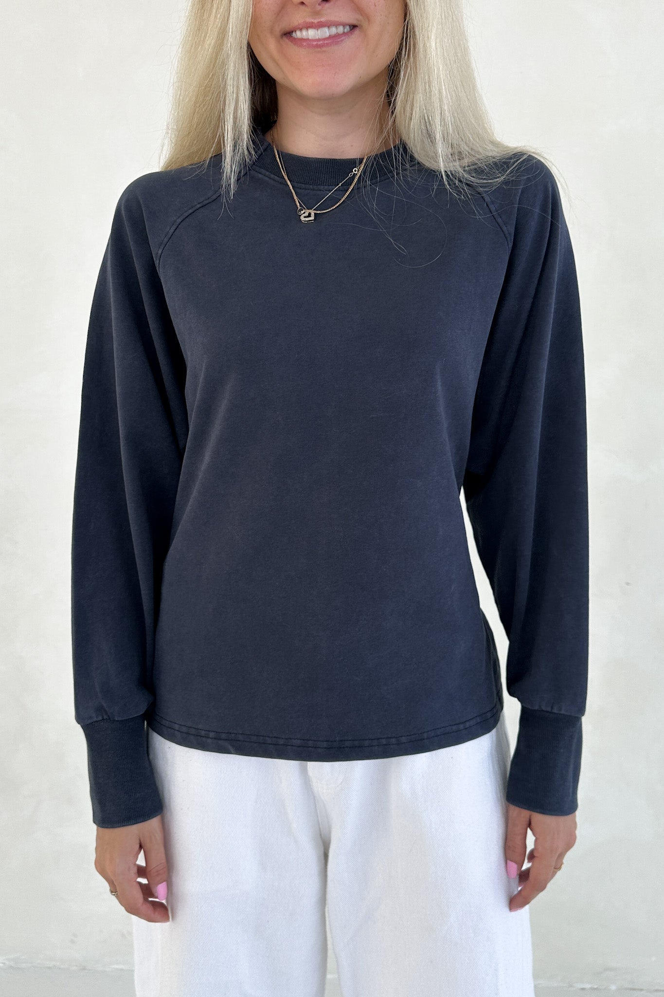 Person wearing a navy long-sleeve top and white pants against a light background