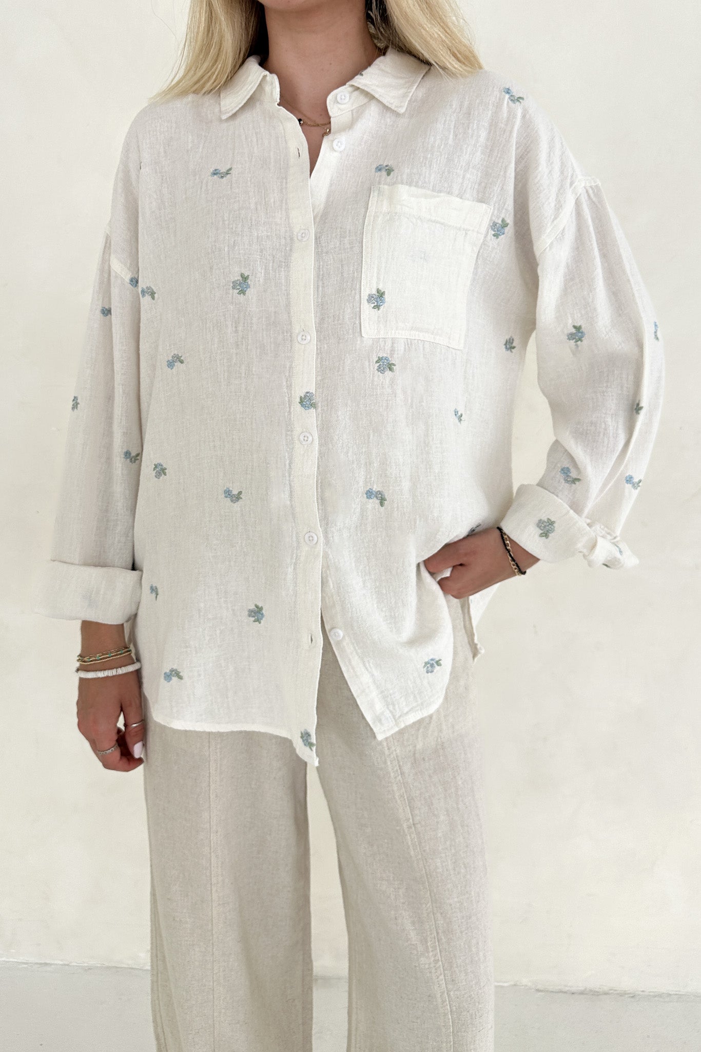 Person wearing a white shirt with subtle pattern and beige pants on a plain background