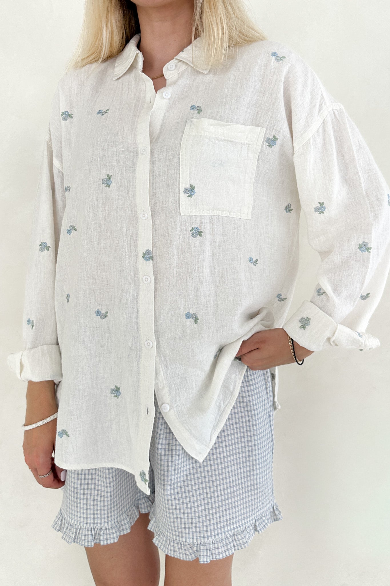 Person wearing a white shirt with small patterns and checkered shorts on a plain background