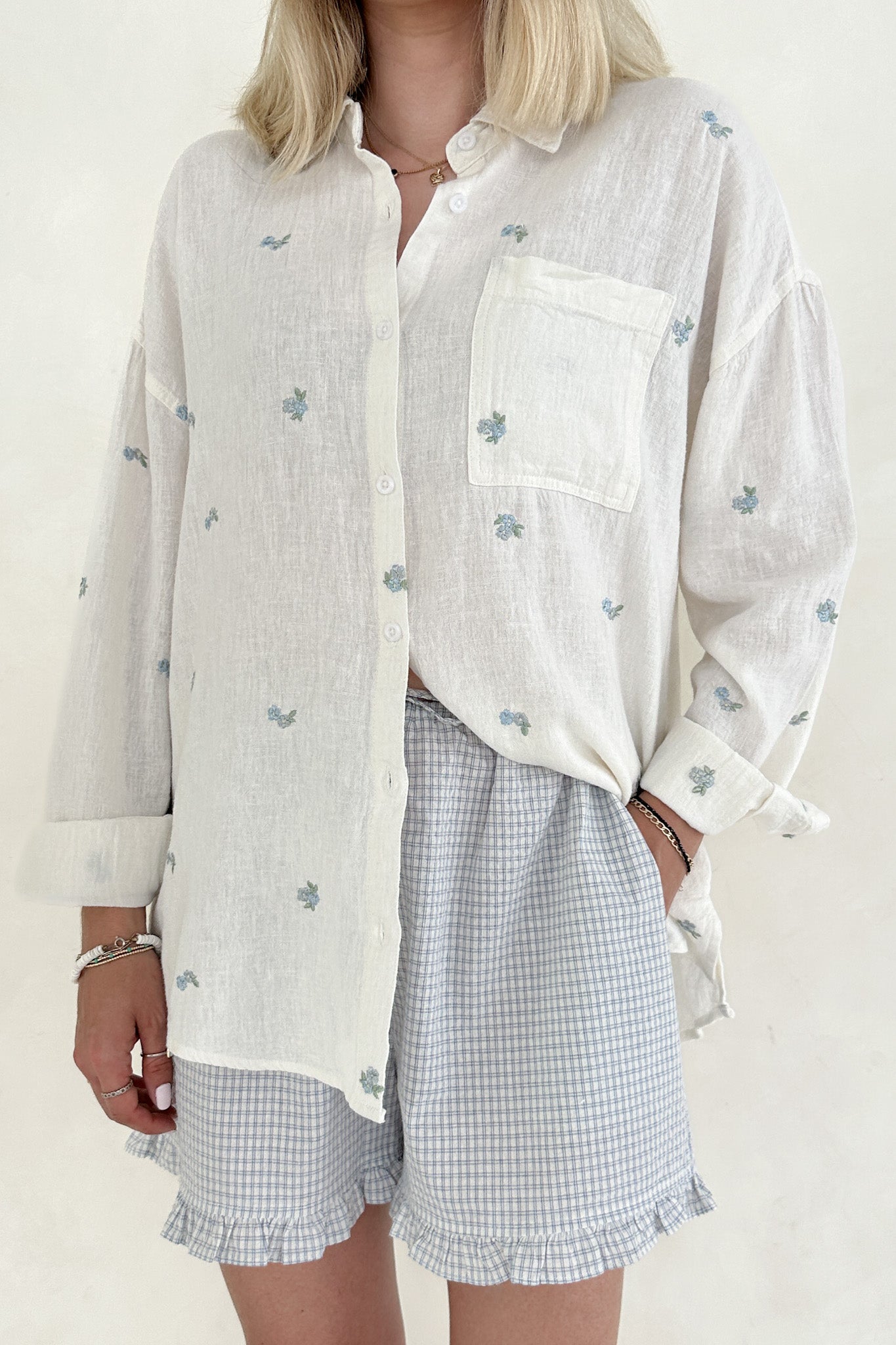 Person wearing a white floral shirt and checkered shorts on a plain background