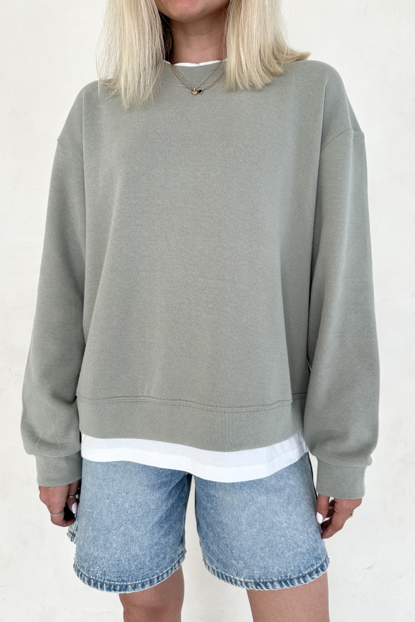 Person wearing a gray sweatshirt and denim shorts on a white background
