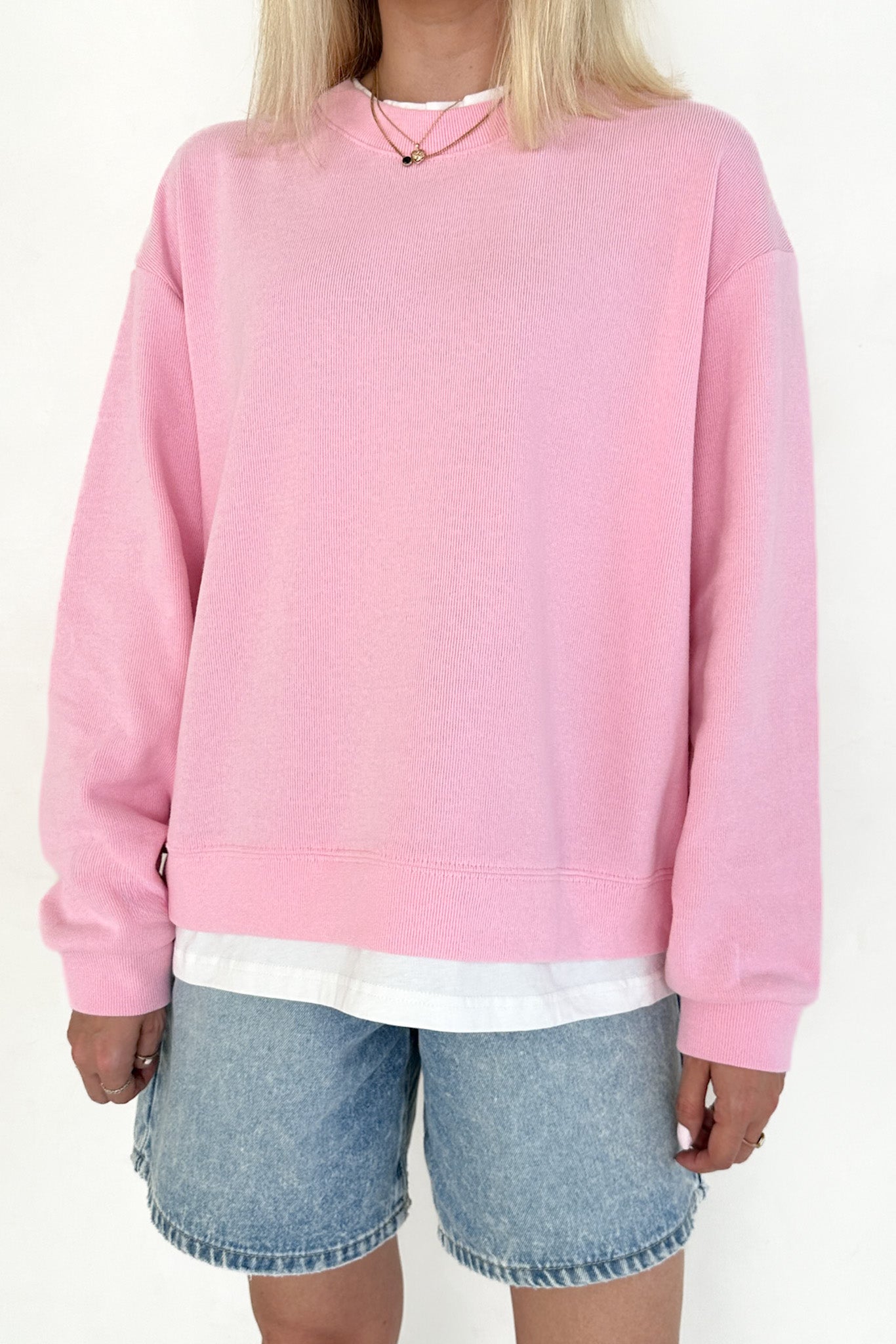 Person wearing a pink sweatshirt and denim shorts on a white background