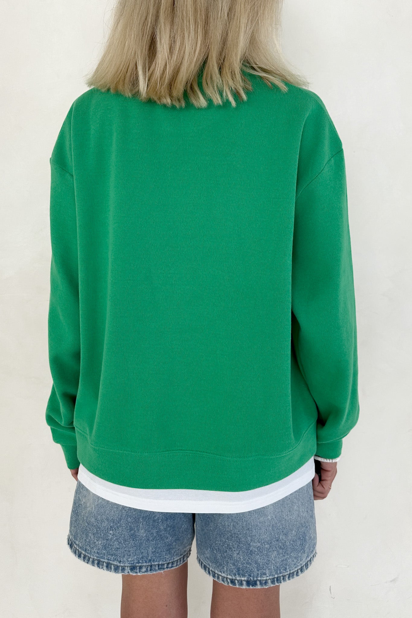 Person wearing a green sweatshirt and denim shorts on a white background