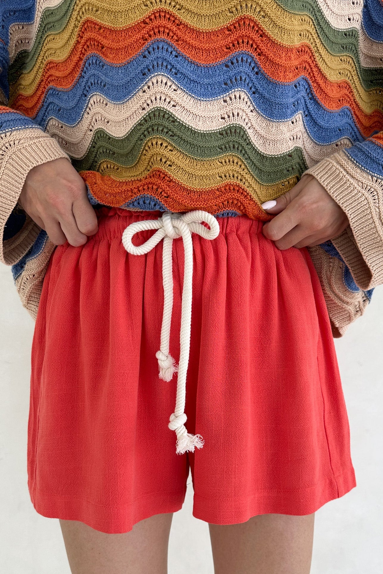 Person wearing a colorful sweater and red shorts with a white background