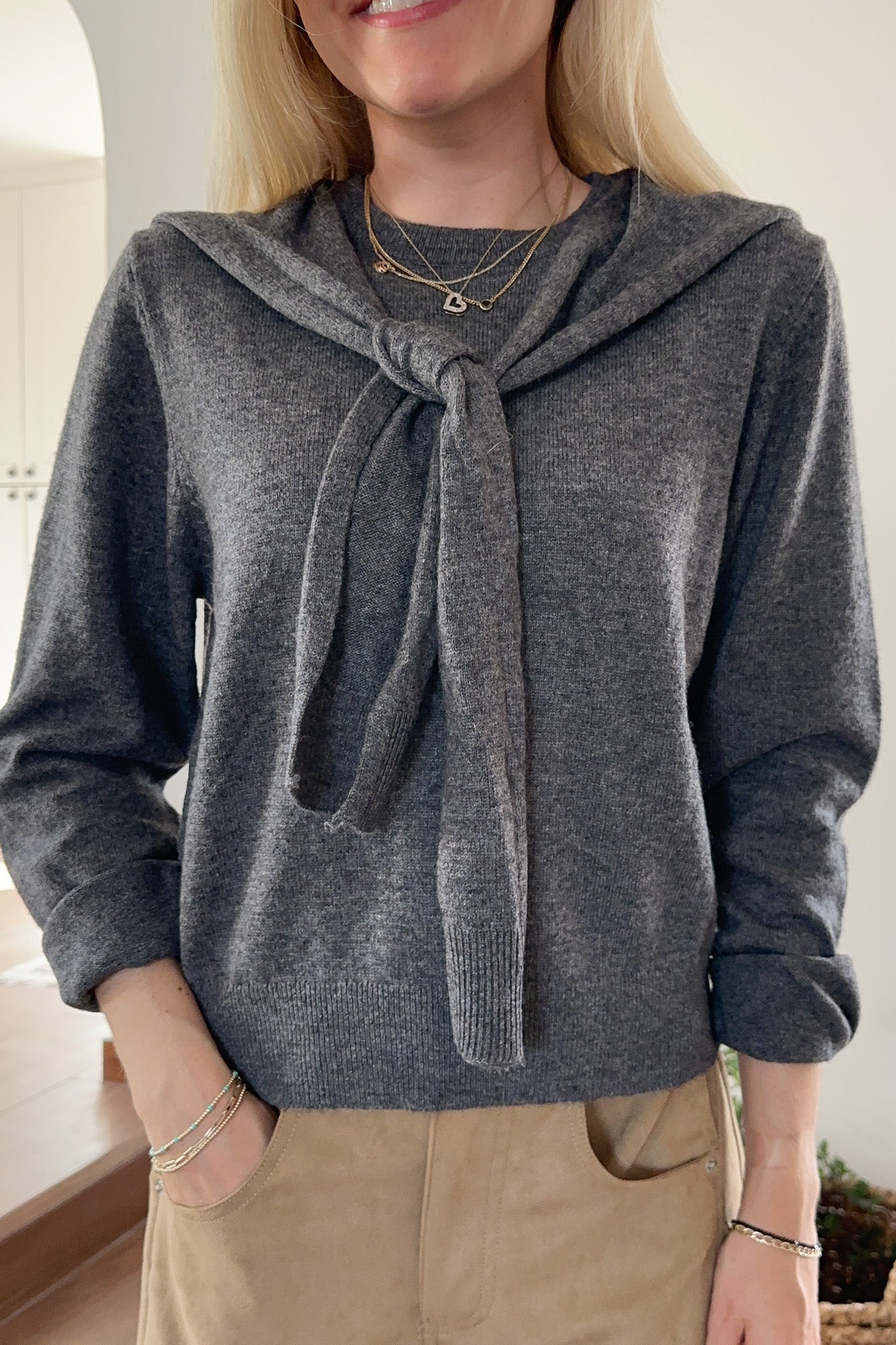 Woman wearing a gray sweater with a tie detail in an indoor setting