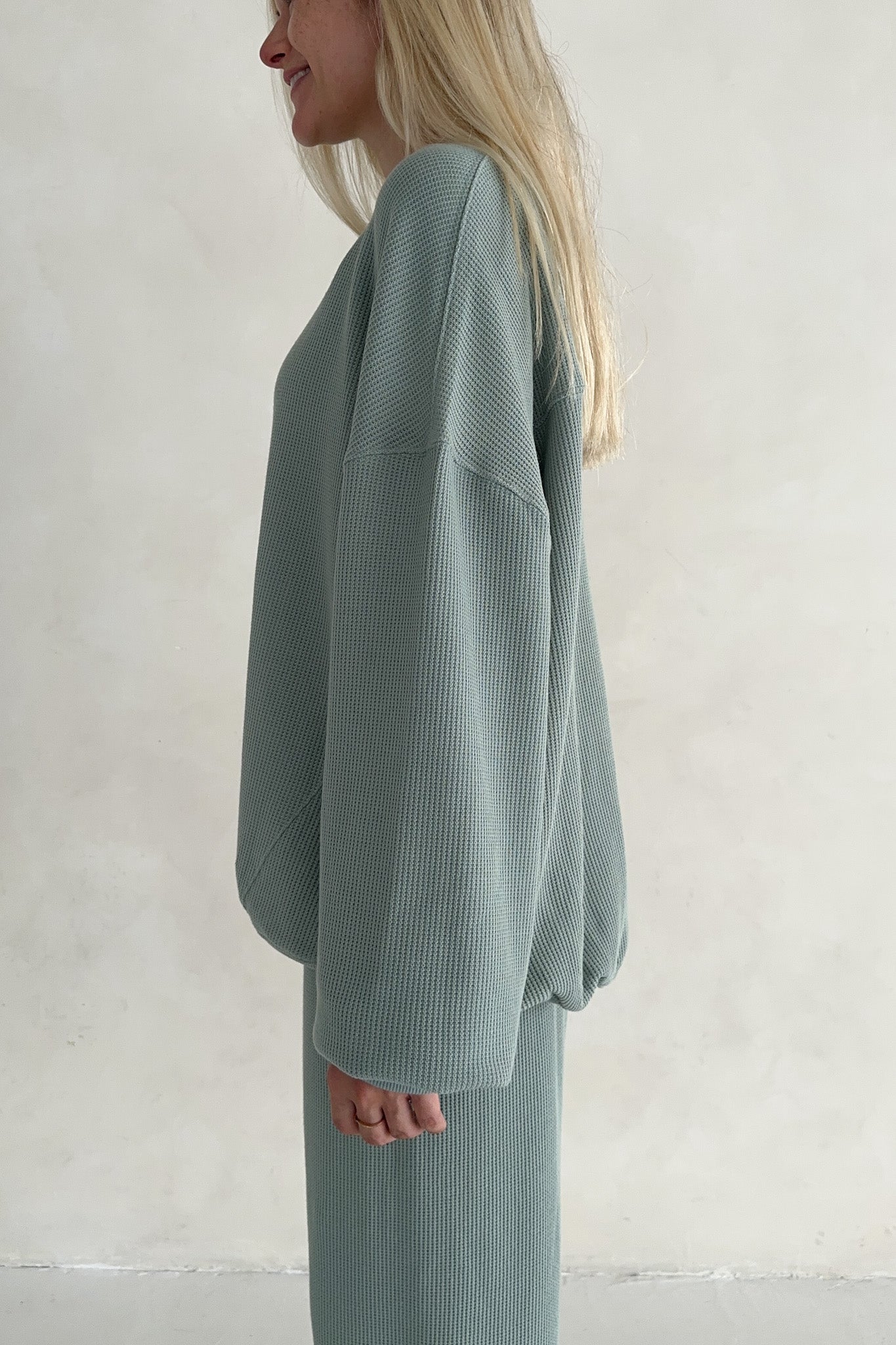 Person wearing a light green textured outfit against a plain background