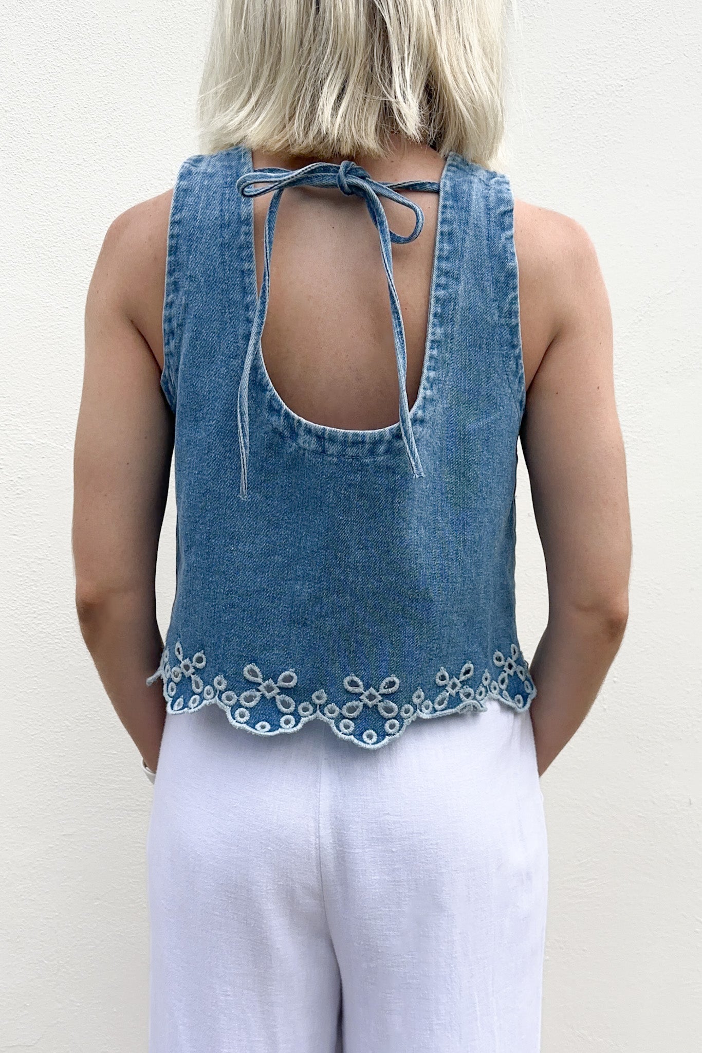 Denim top with floral embroidery and white pants on a plain background