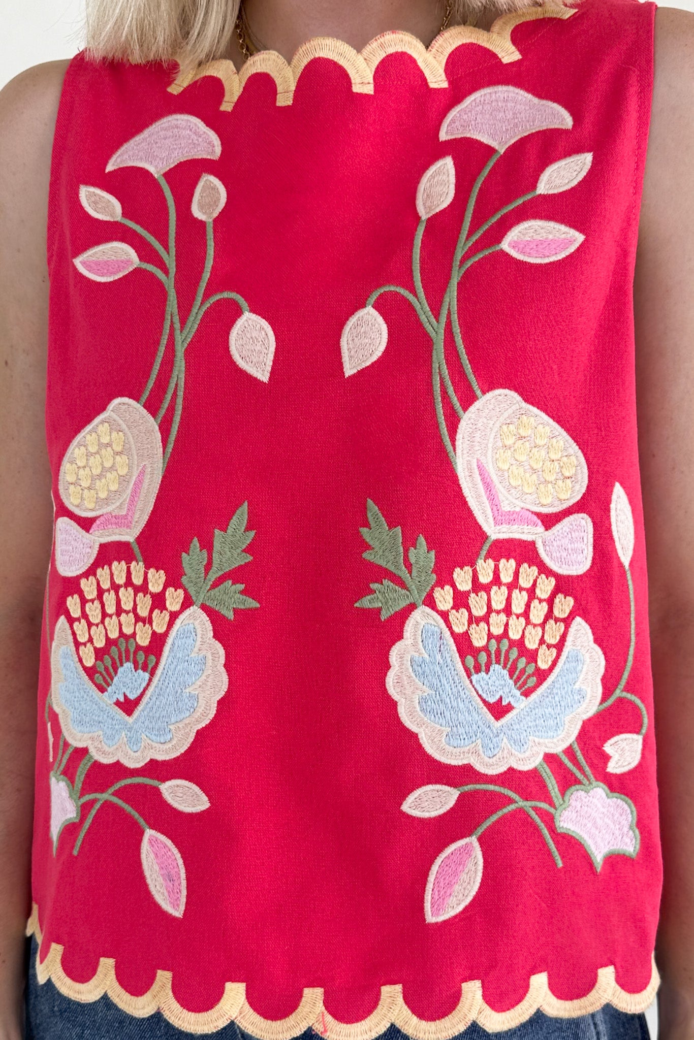 Red sleeveless top with floral embroidery on a person wearing it.
