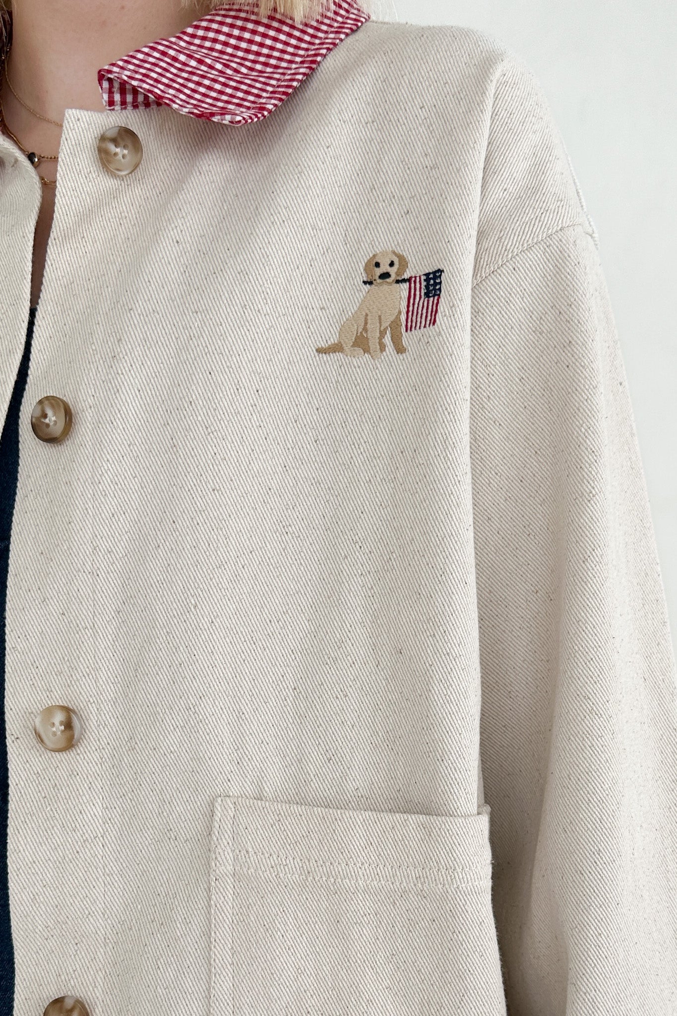 Close-up of a beige coat with a dog embroidered patch on the chest.