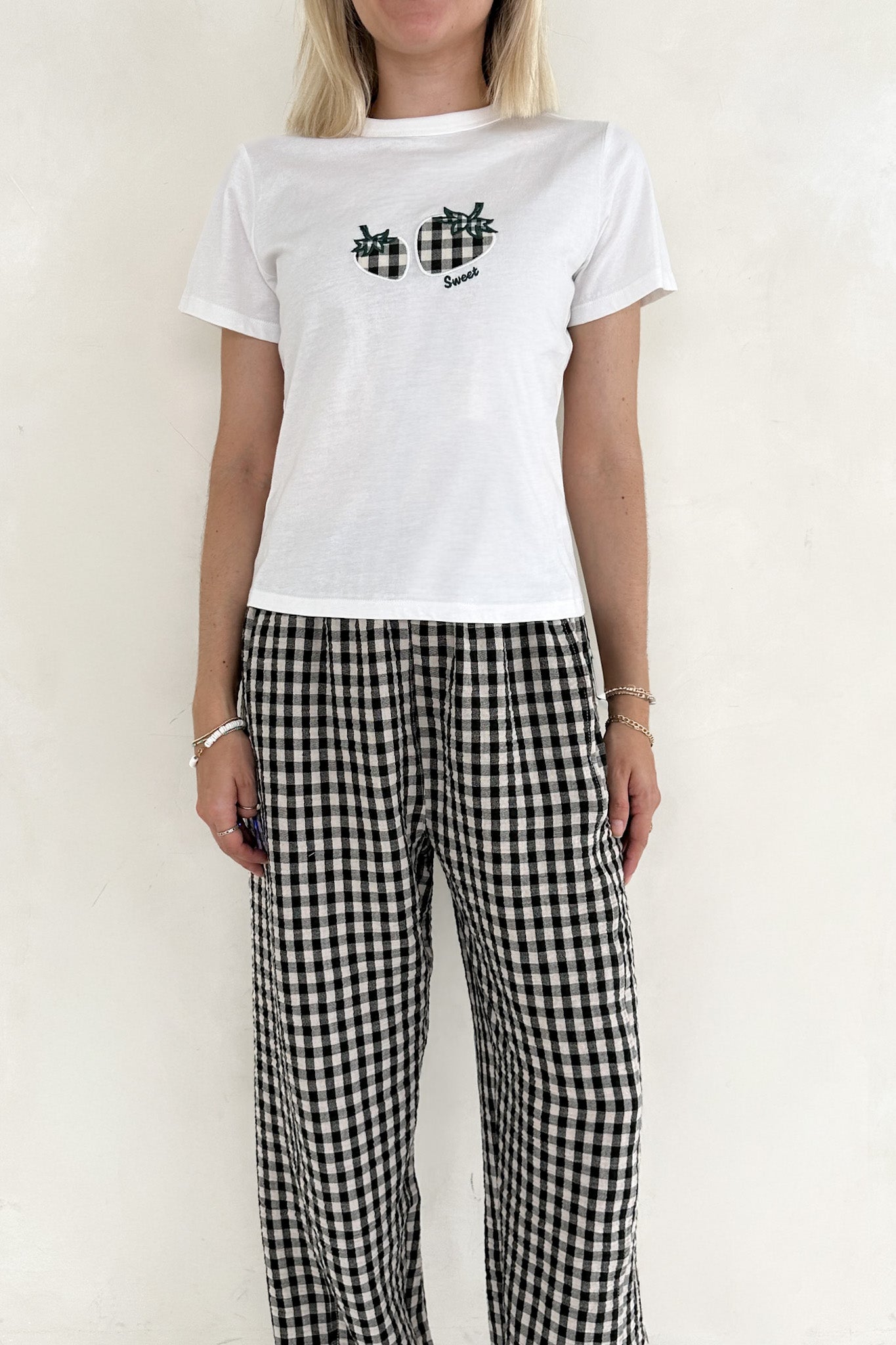 Person wearing a white t-shirt with black design and checkered pants on a plain background
