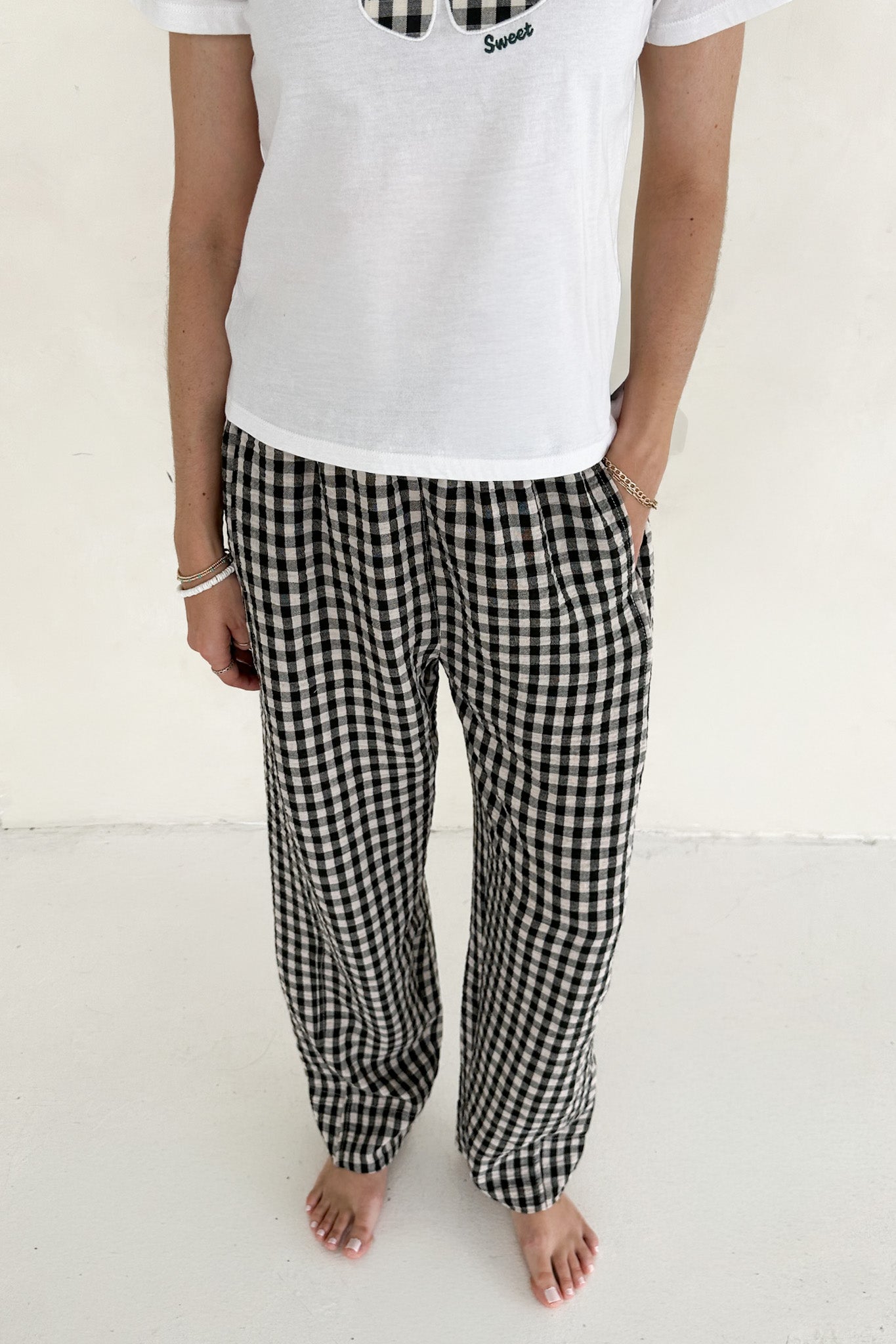 Person wearing a white t-shirt and black and white checkered pants on a plain background