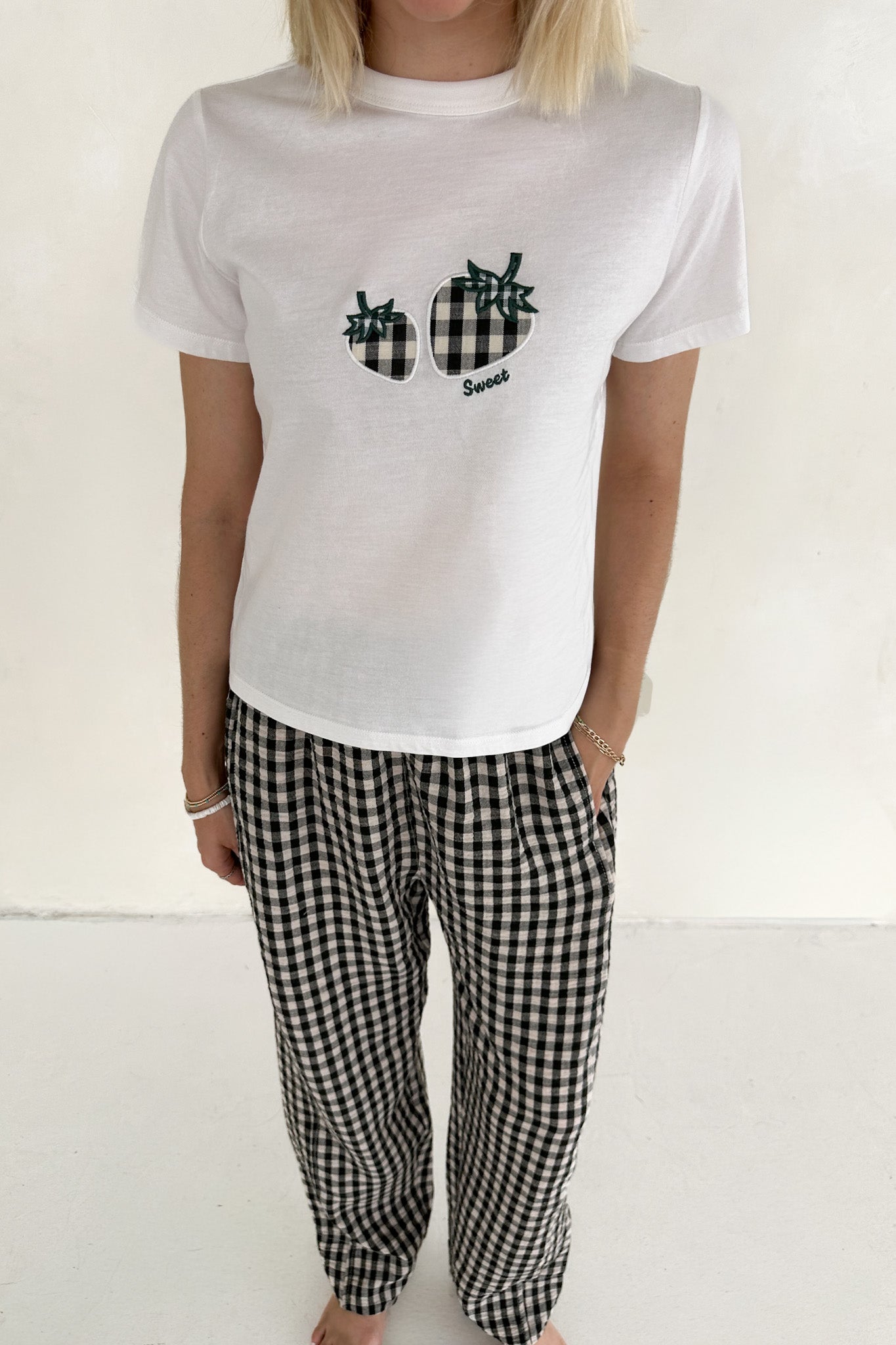 Person wearing a white t-shirt with a graphic design and black and white checkered pants on a plain background