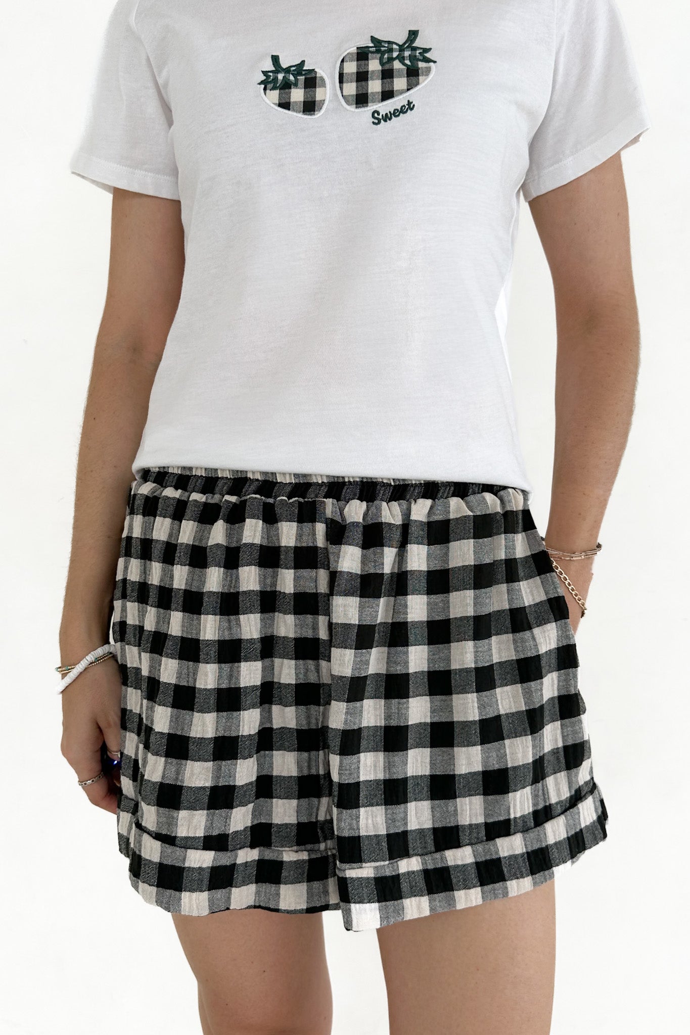 Person wearing a white t-shirt with sunglasses graphics and text, paired with black and white checkered shorts on a white background.
