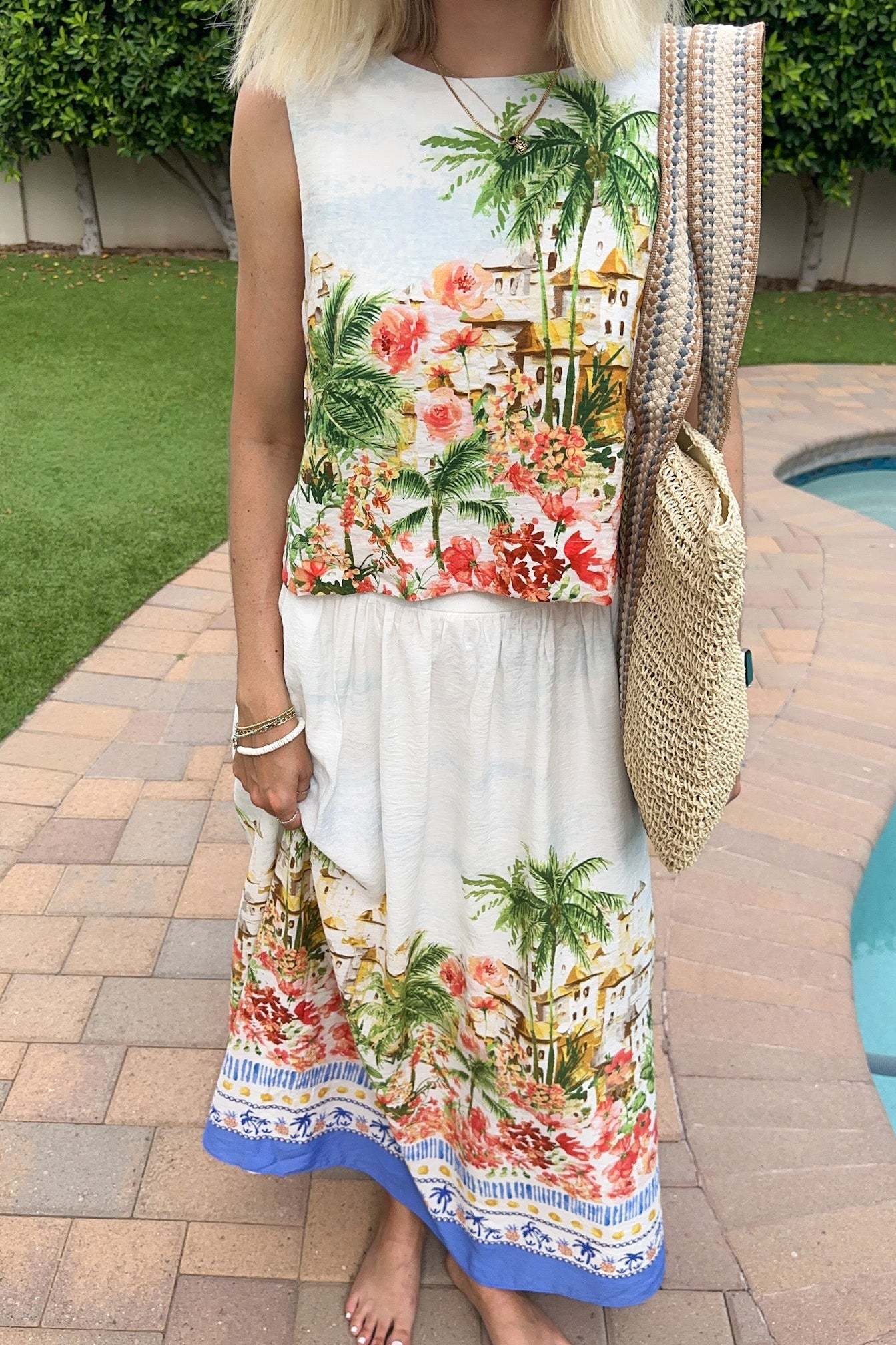 Woman wearing a colorful dress with palm tree and floral design, standing by a pool.