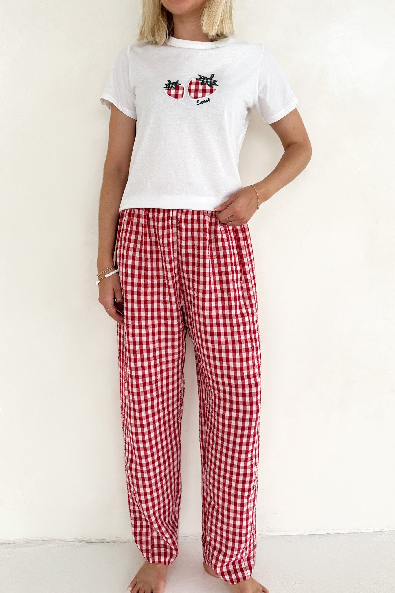 Person wearing a white t-shirt with a graphic design and red checkered pants against a white background