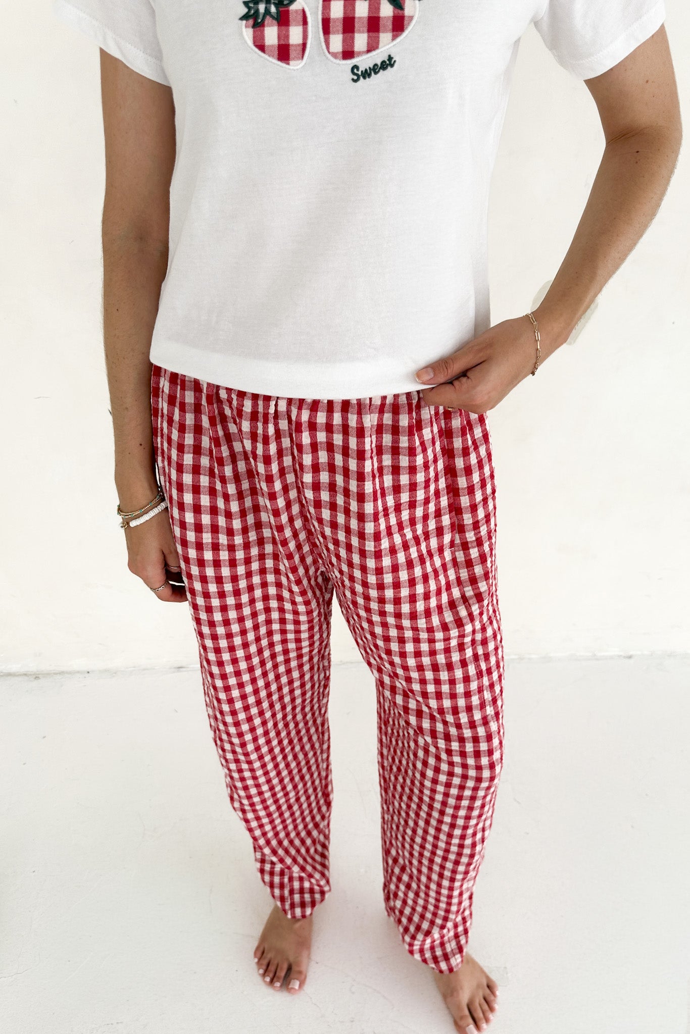 Person wearing a white t-shirt with a graphic design and red checkered pants on a white background
