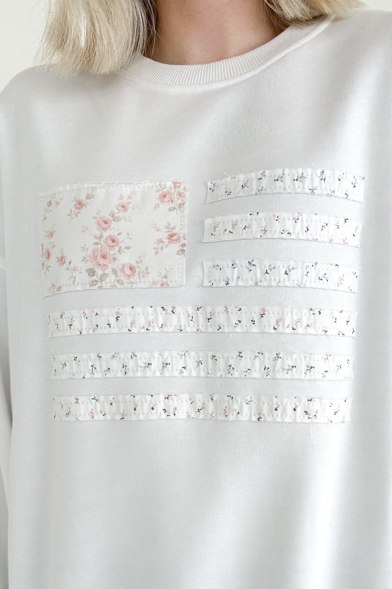 White sweater with floral and lace details on a plain background