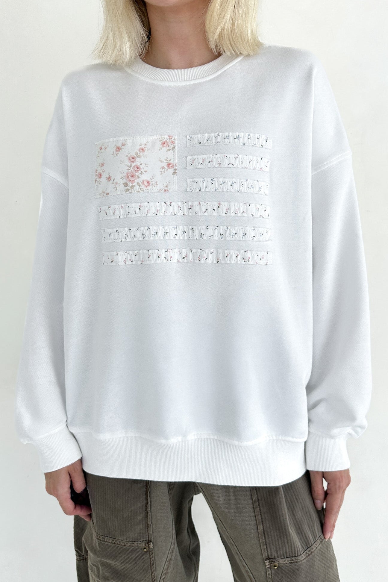 White sweatshirt with lace details worn by a person on a plain background