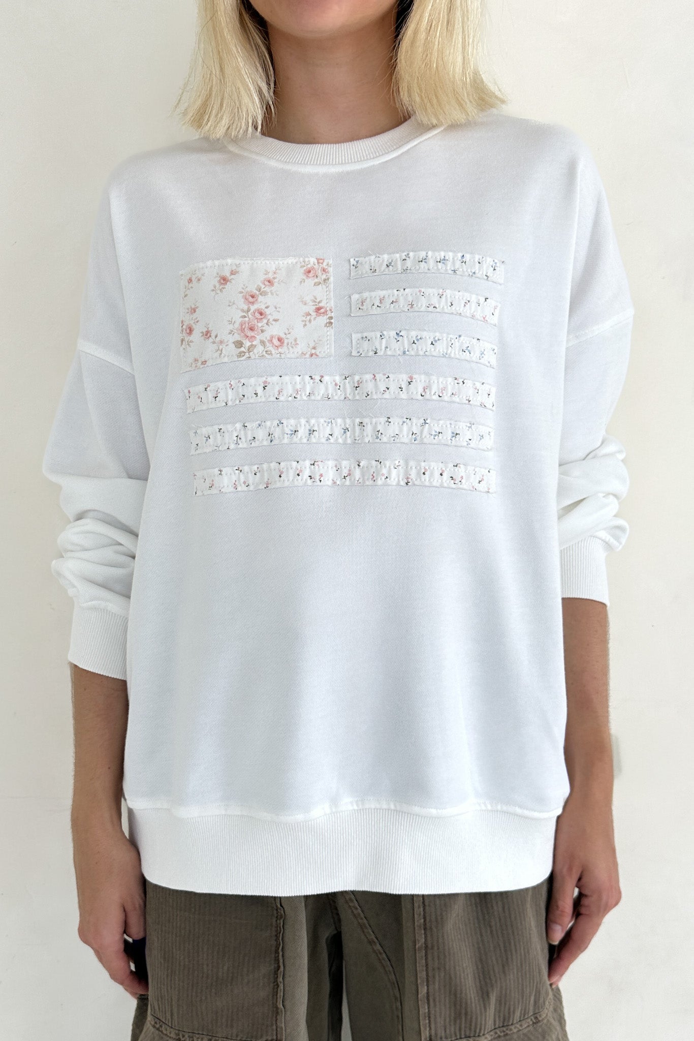 White sweatshirt with lace details and floral design on a plain background