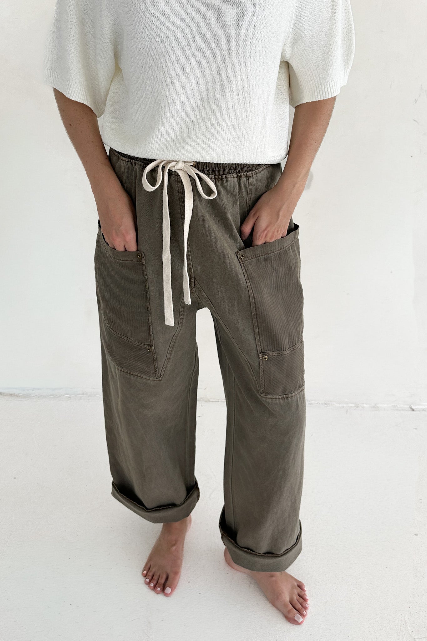Person wearing olive green pants with a white drawstring on a white background
