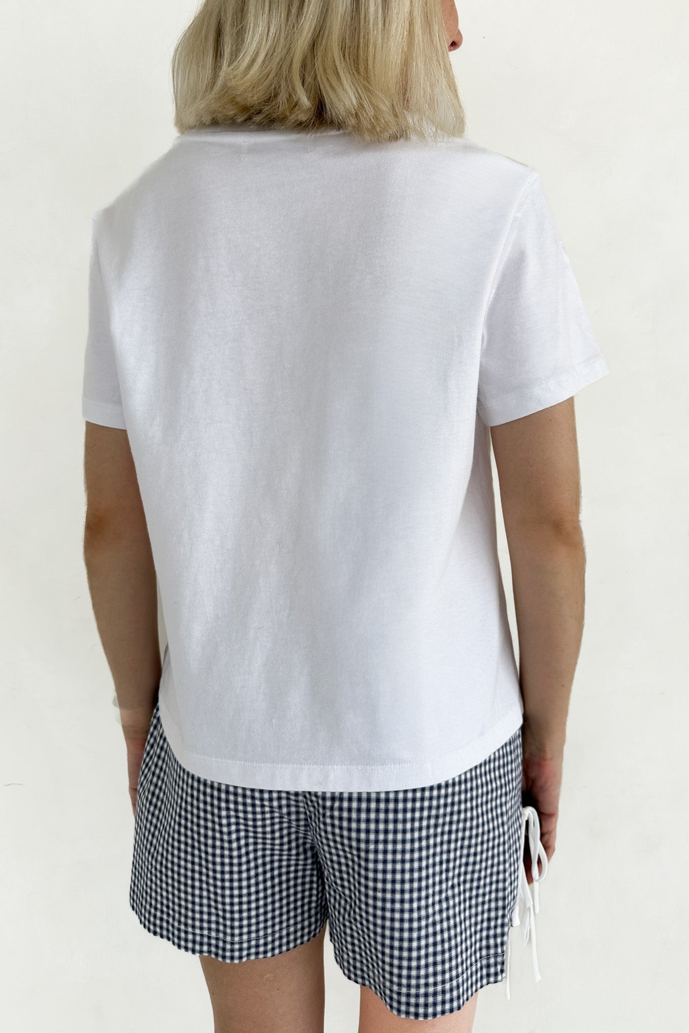 Person wearing a white t-shirt and checkered shorts on a plain background