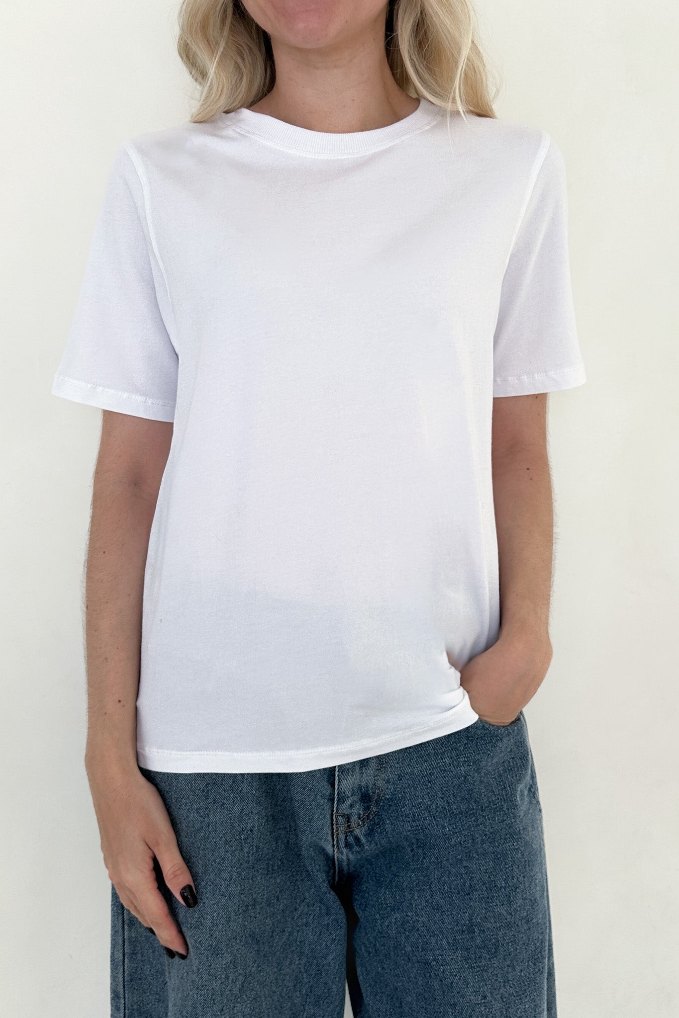 Person wearing a plain white t-shirt and blue jeans against a light background