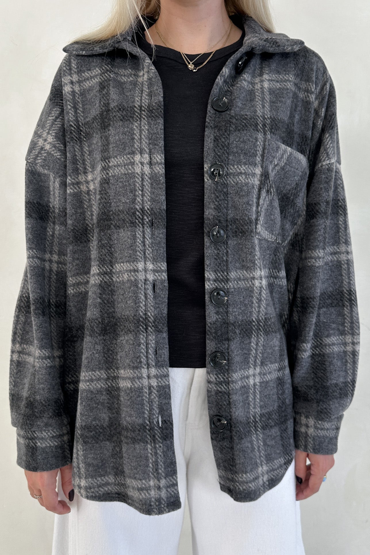 Person wearing a gray plaid shirt with a hood against a plain background