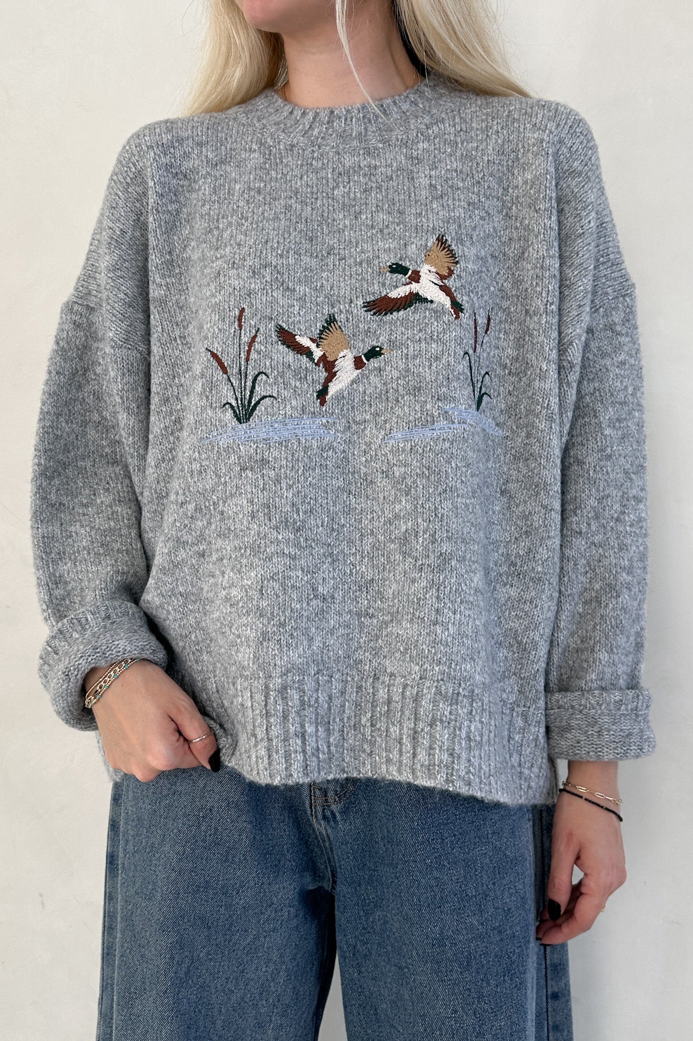 Person wearing a gray sweater with bird embroidery on a plain background