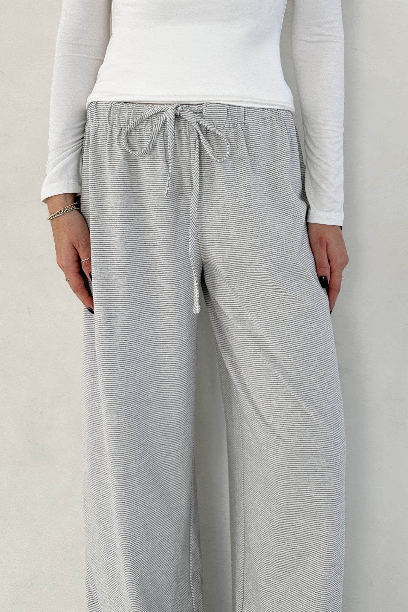 Person wearing gray striped pants and a white top against a plain background