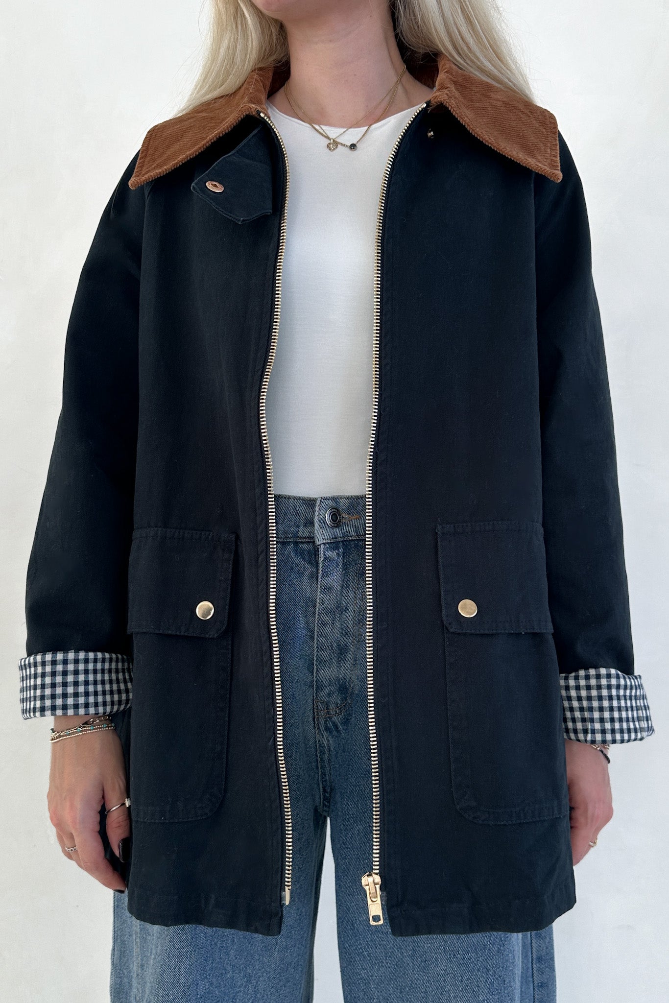 Person wearing a black jacket with brown collar and checkered cuffs on a white background