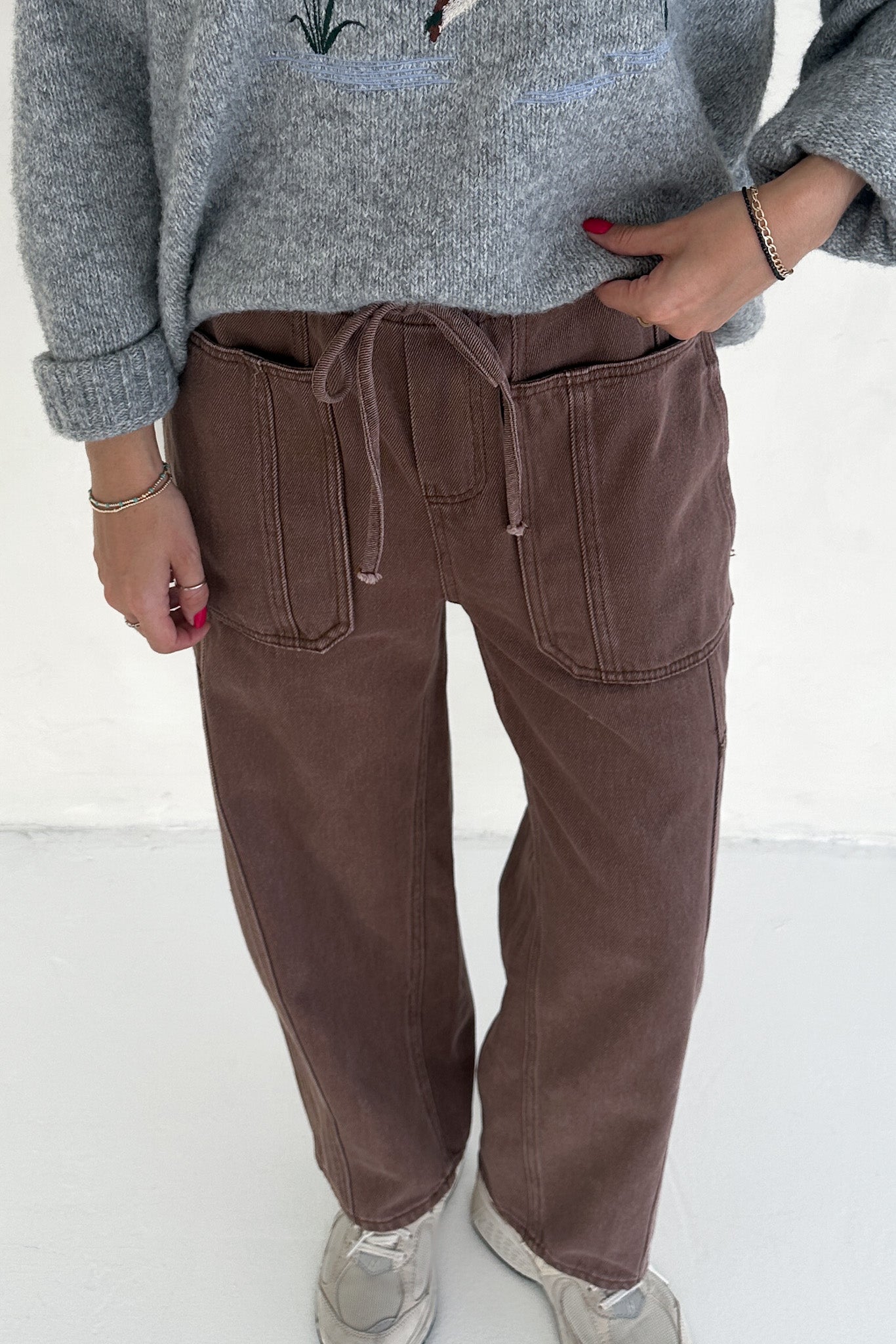 Person wearing brown pants and a gray sweater on a white background