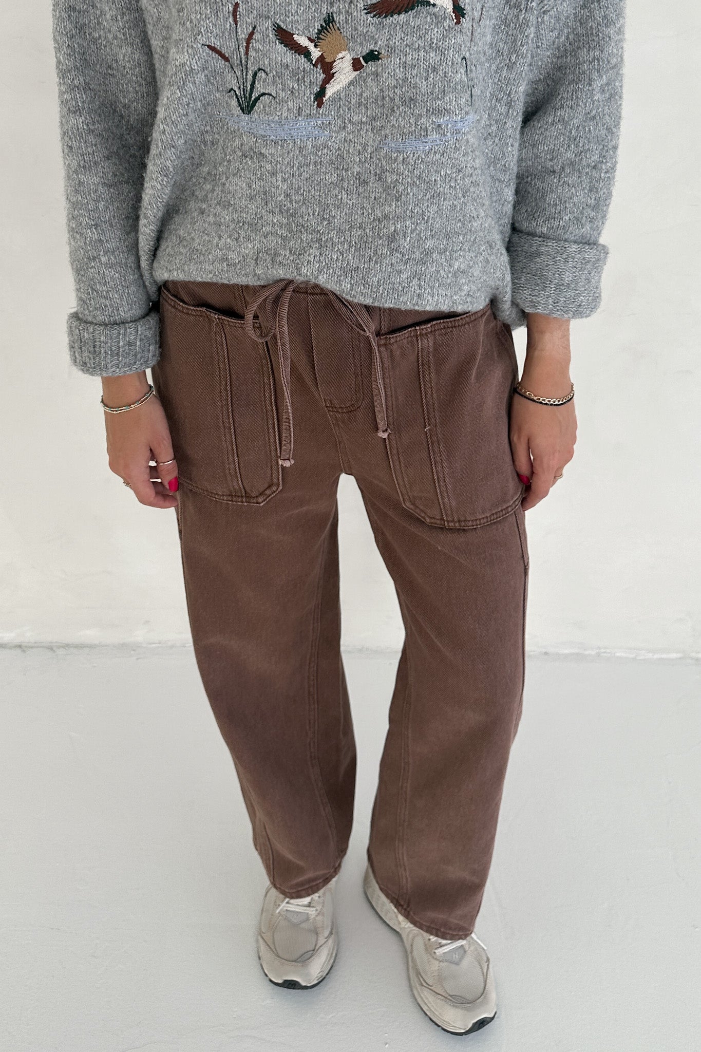 Person wearing a gray sweater with bird design and brown pants on a white background