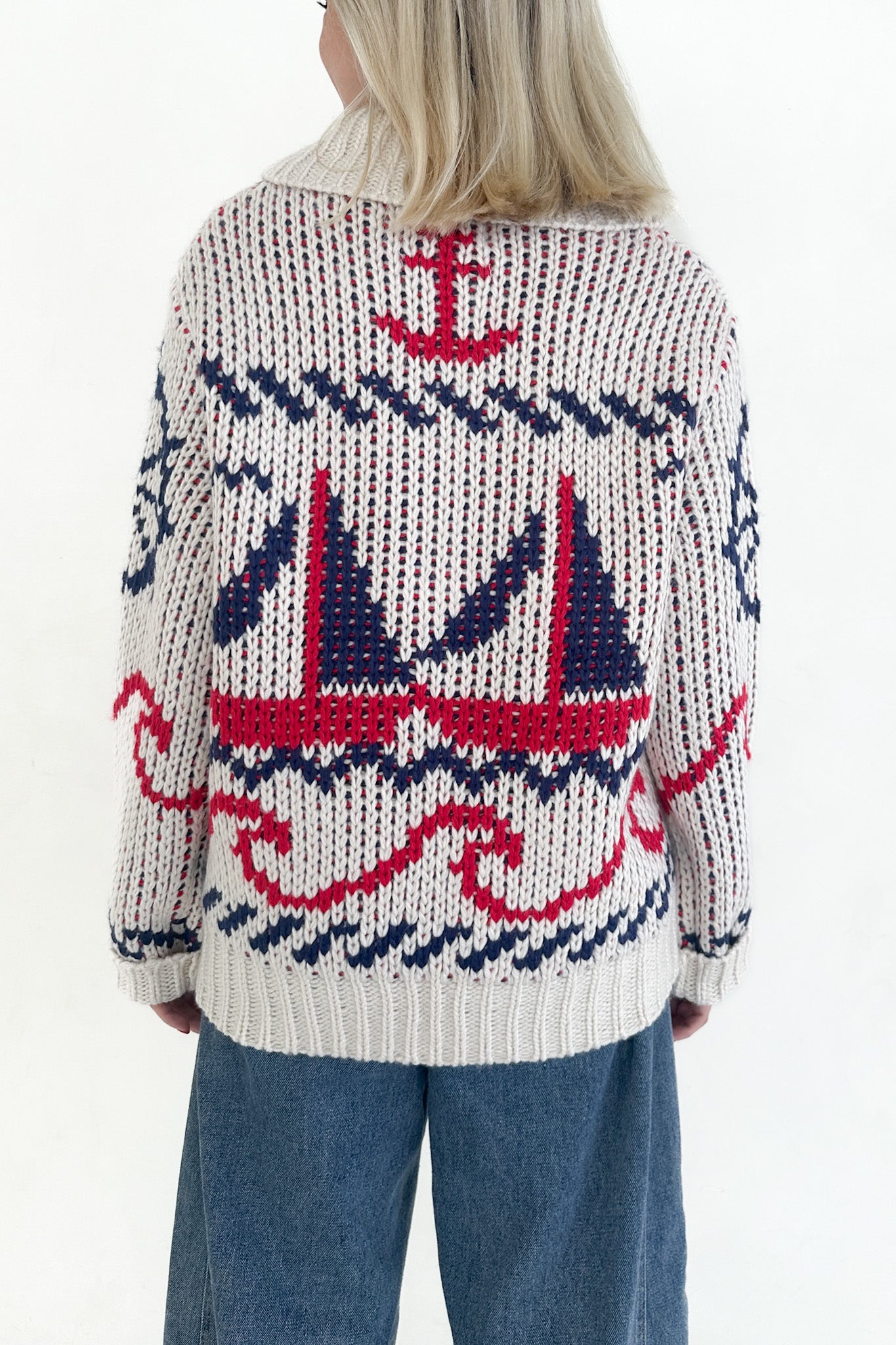 Person wearing a knitted sweater with nautical patterns on a white background