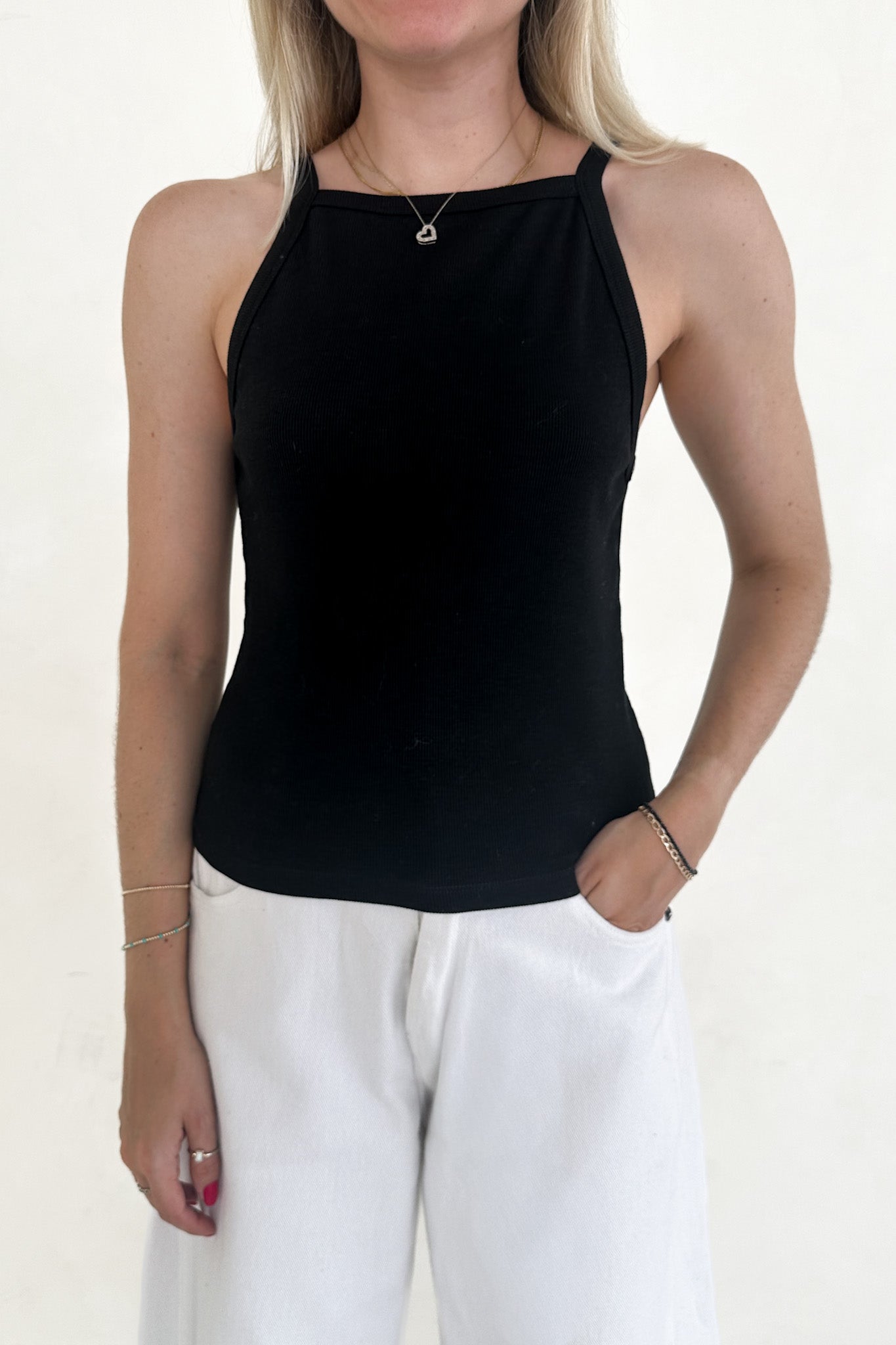 Person wearing a black sleeveless top and white pants on a plain background