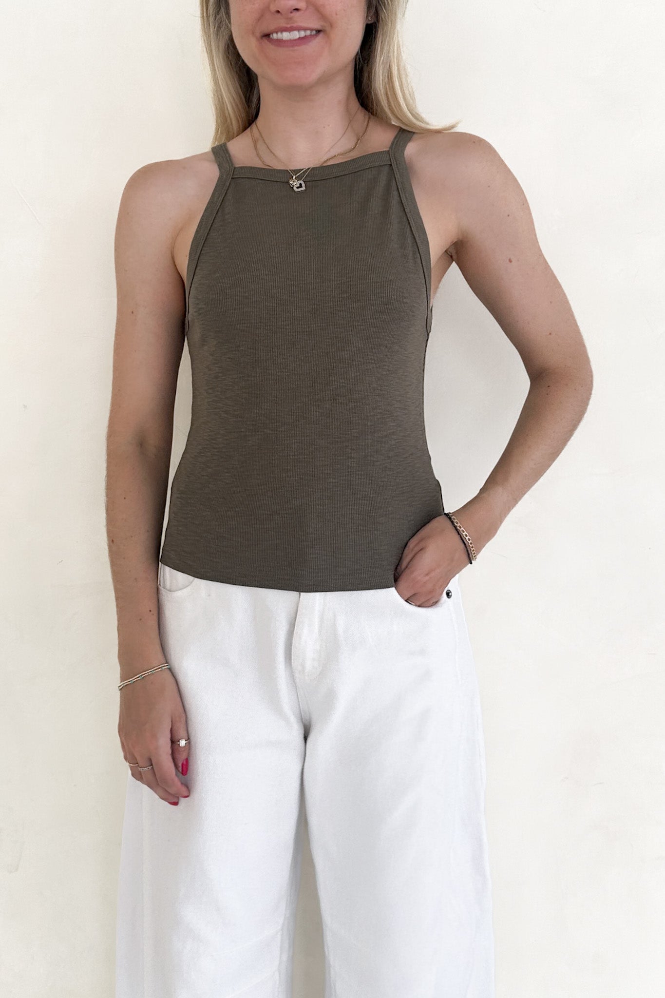 Woman wearing a green tank top and white pants against a plain background