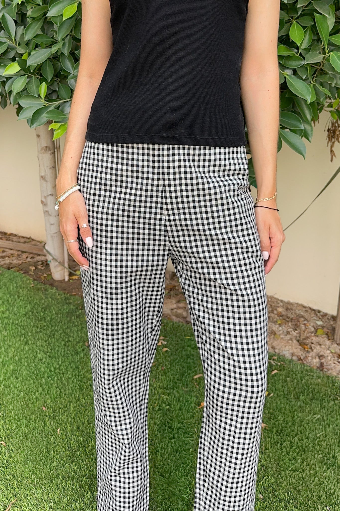 Person wearing black and white checkered pants standing on grass with greenery in the background