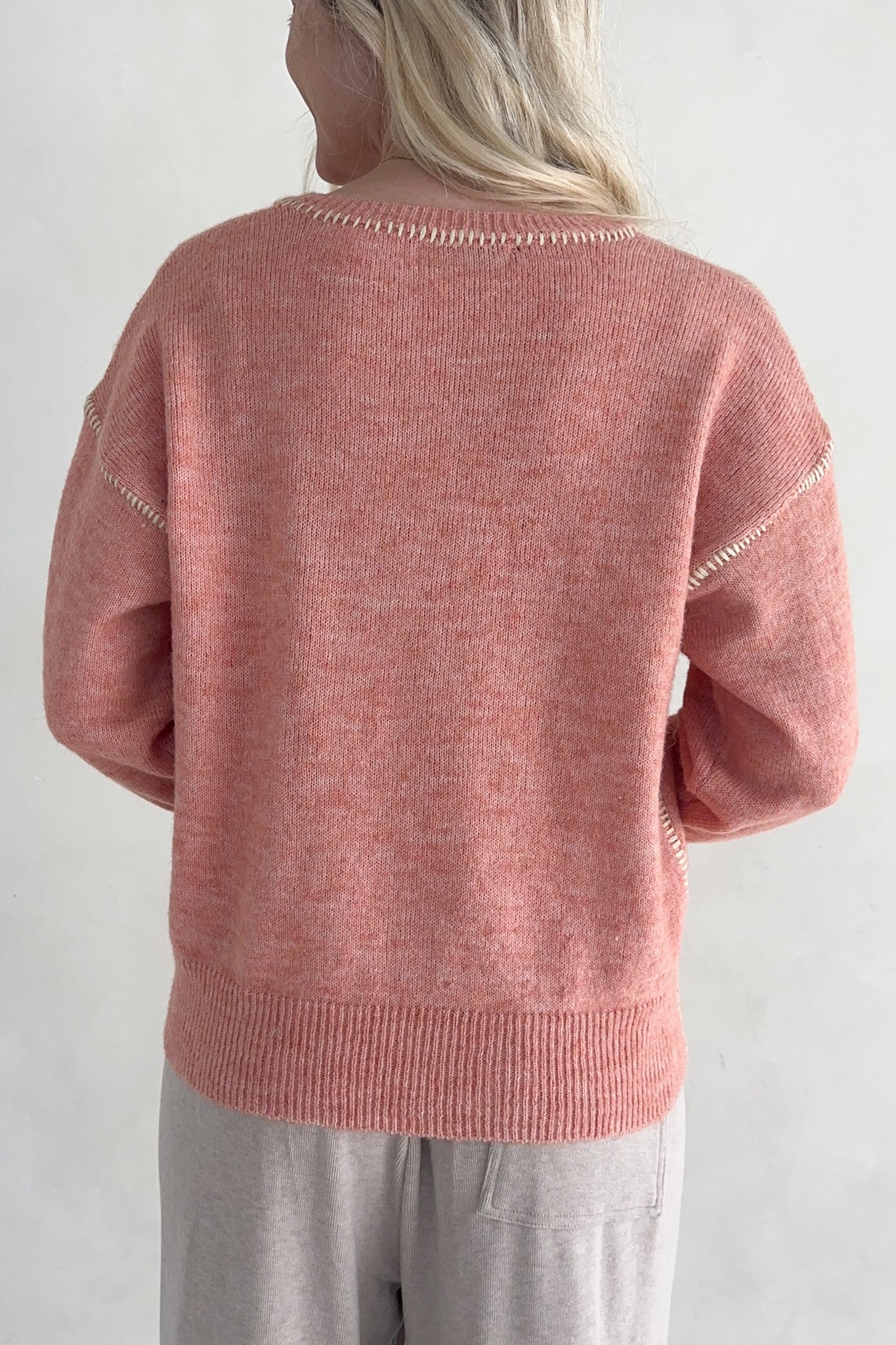 Person wearing a pink knitted sweater with white trim on a plain background