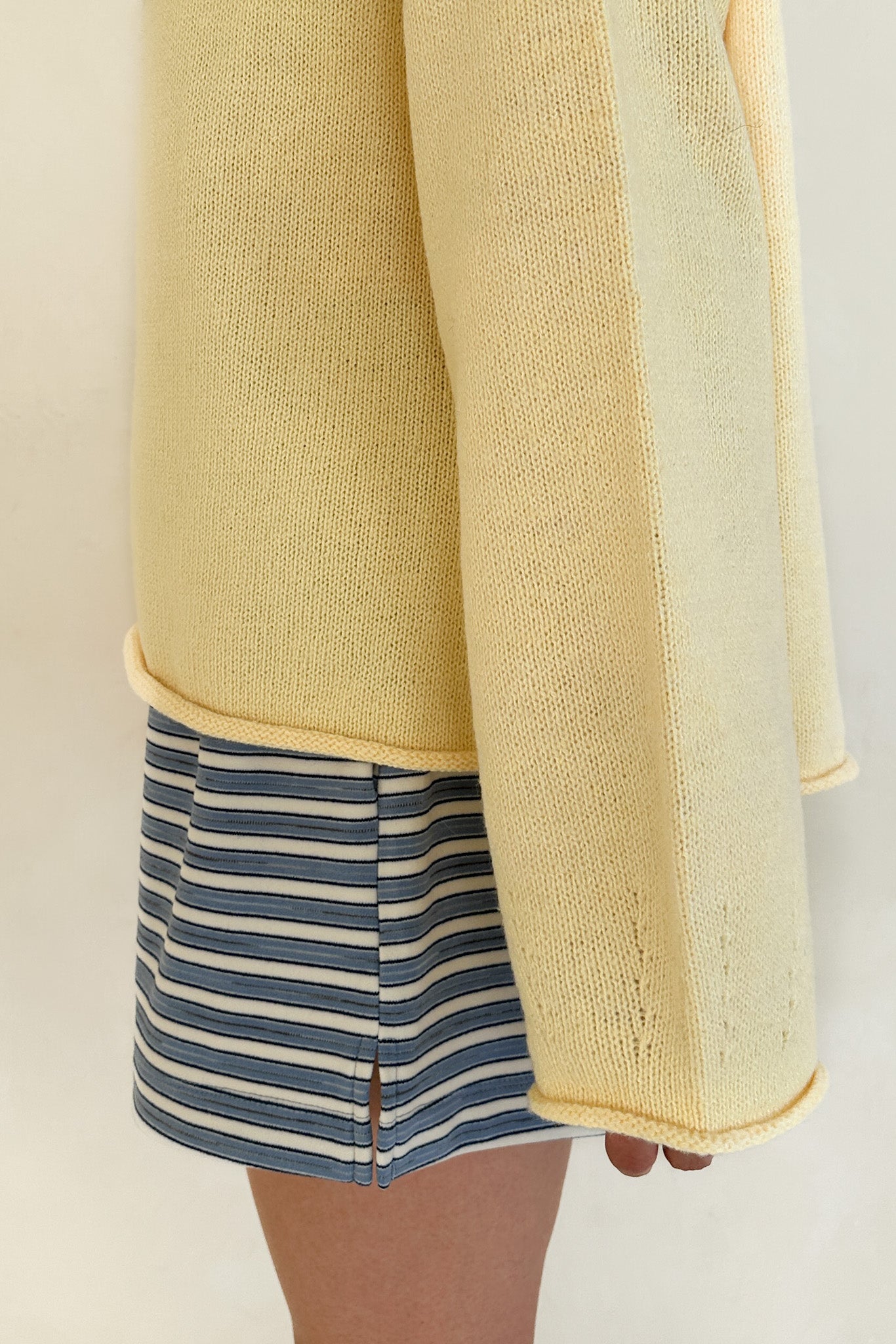 Yellow knit cardigan over a striped garment on a neutral background